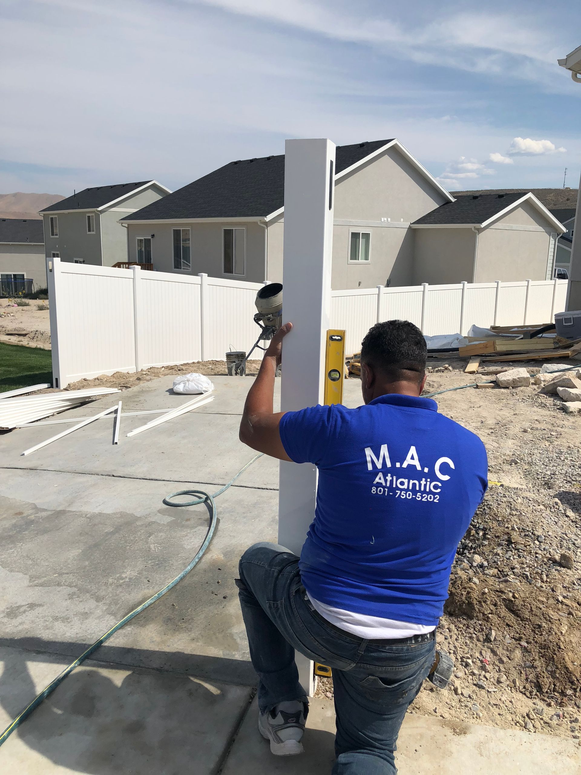 A man in a blue shirt is kneeling down next to a white pole.