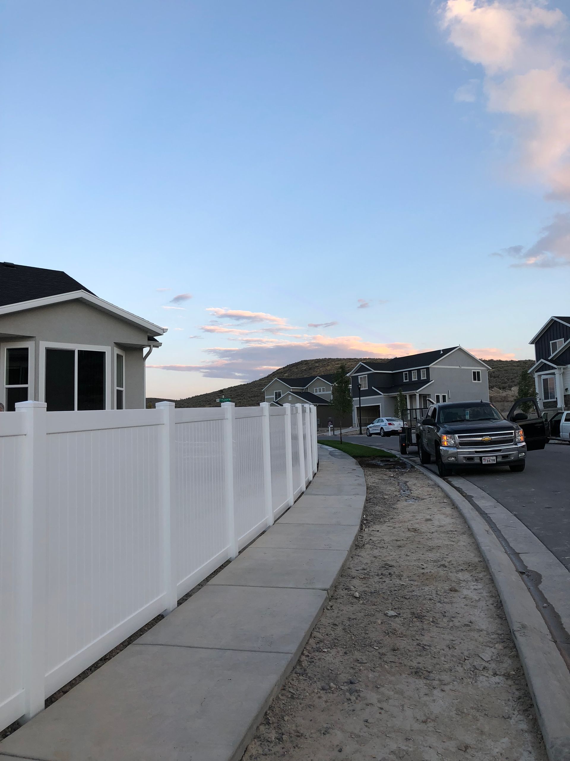 A white fence surrounds a sidewalk in a residential area.