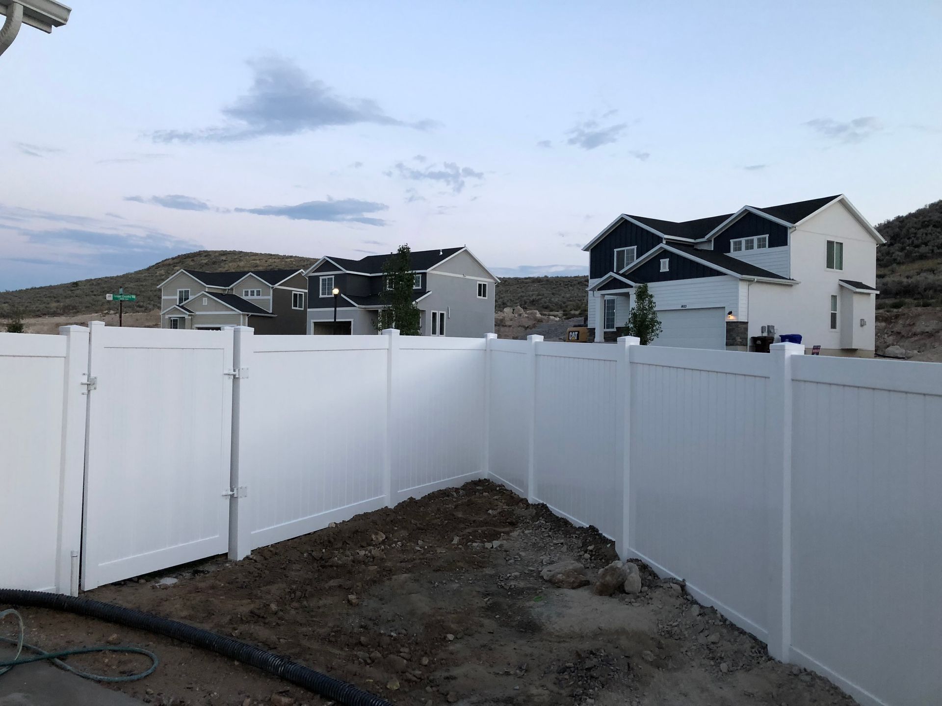 A white fence surrounds a yard with a house in the background.