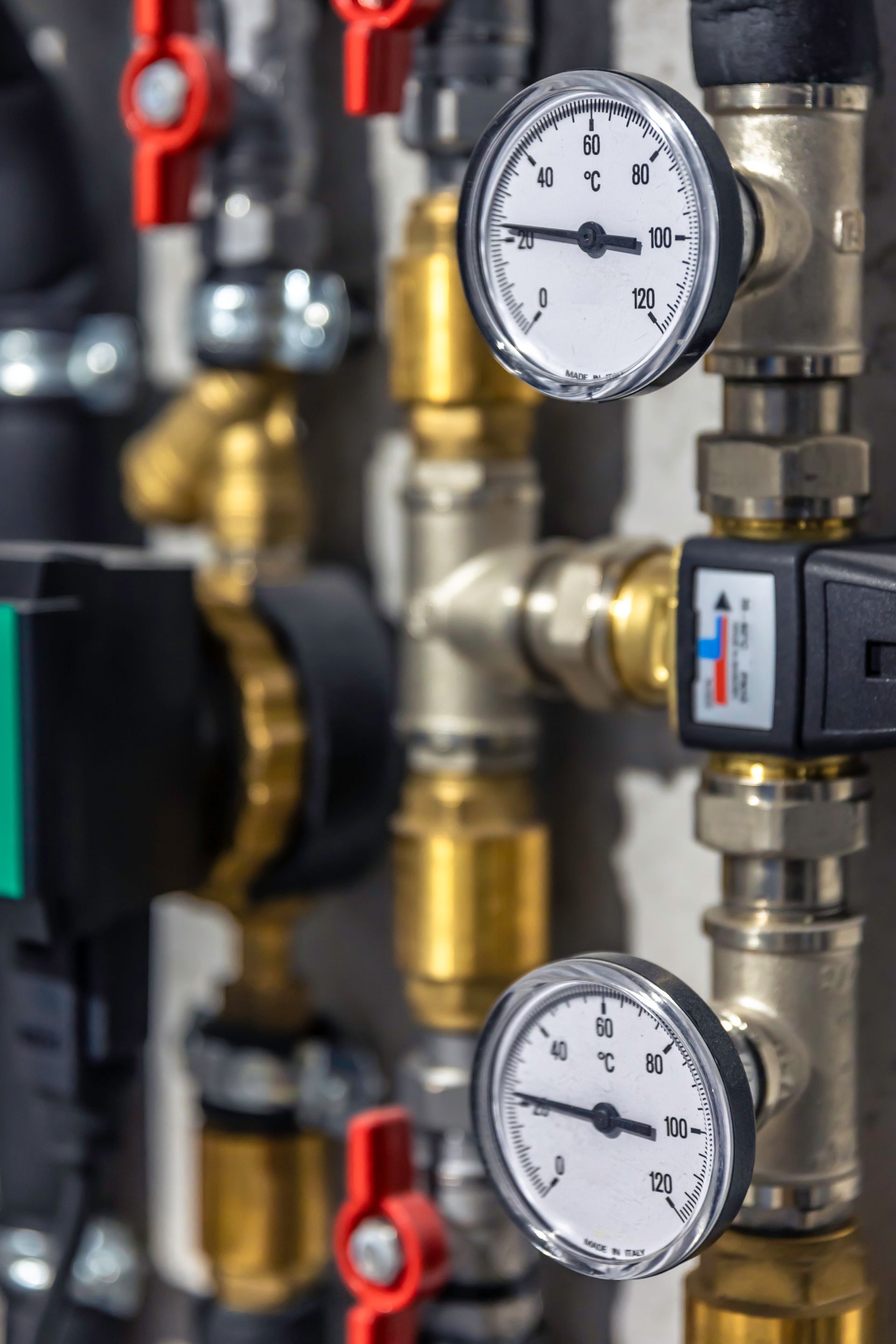 Industrial pipes with two pressure gauges, red valves, and brass fittings in a mechanical room