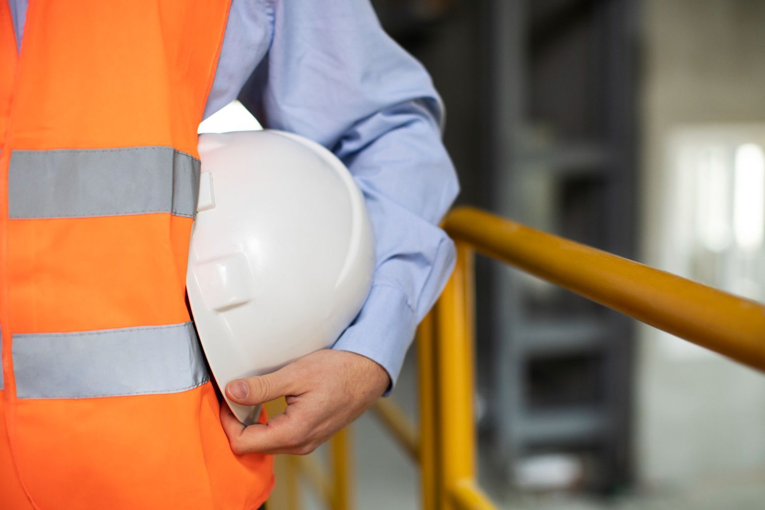 A man in an orange vest is holding a white hard hat.