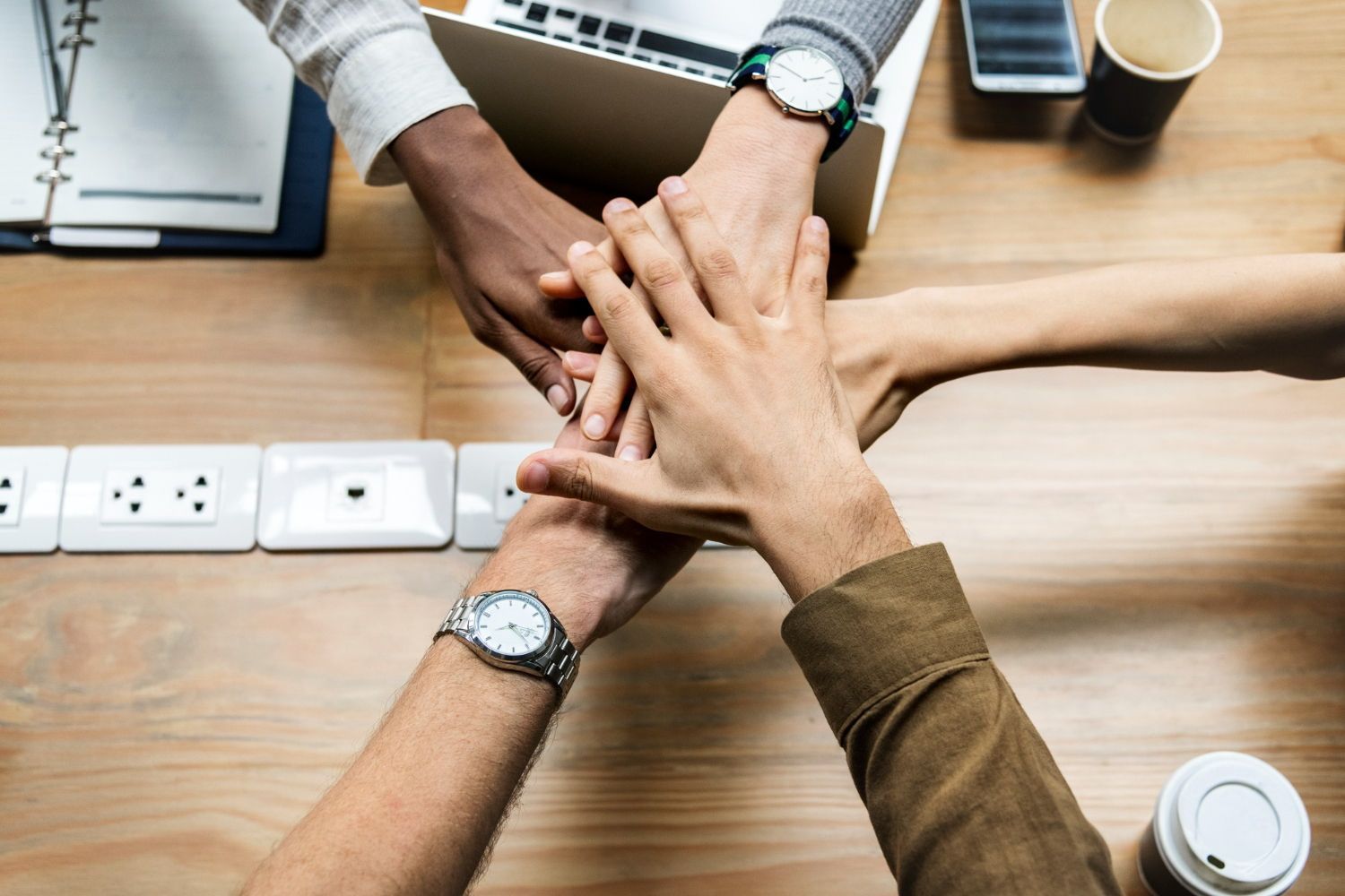 A group of people are putting their hands together on a wooden table.