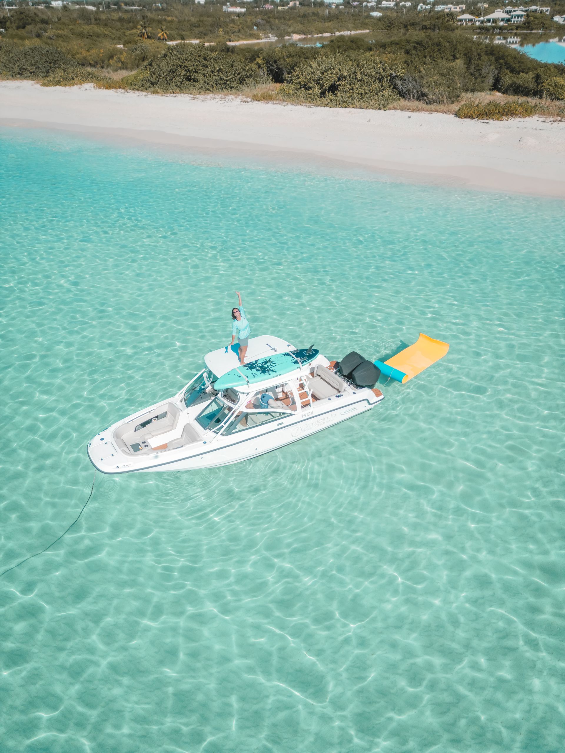 Boat floats in turquoise water near a white sand beach. Green vegetation in the background.