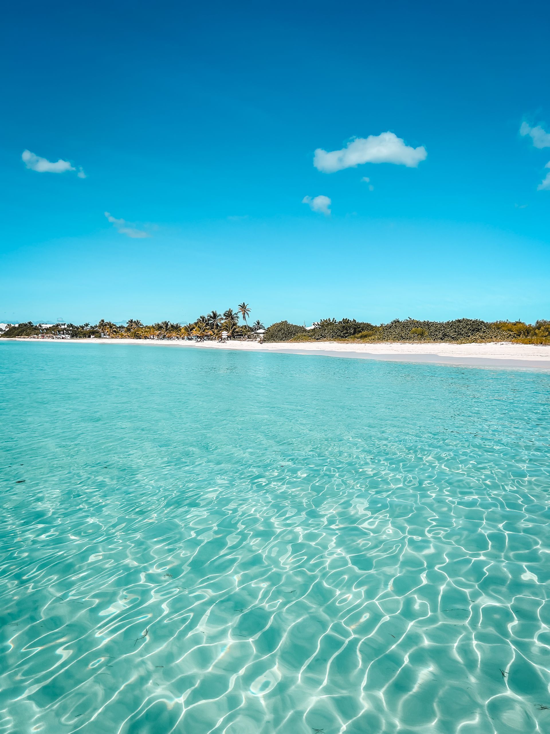 Vibrant turquoise water meets white sand beach under a clear, blue sky with a few clouds.