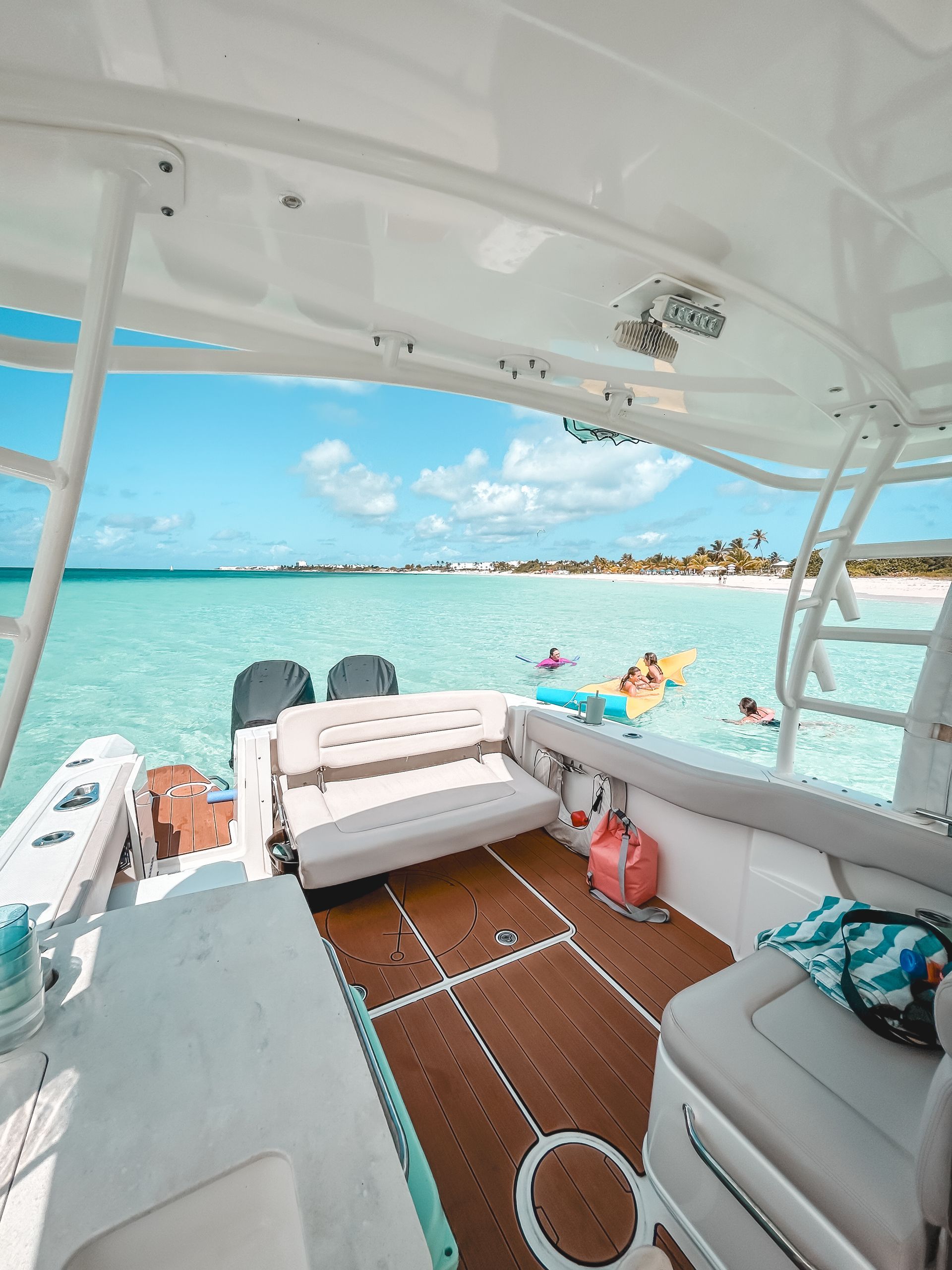 Boat on clear turquoise water with people swimming; sunny day at the beach.
