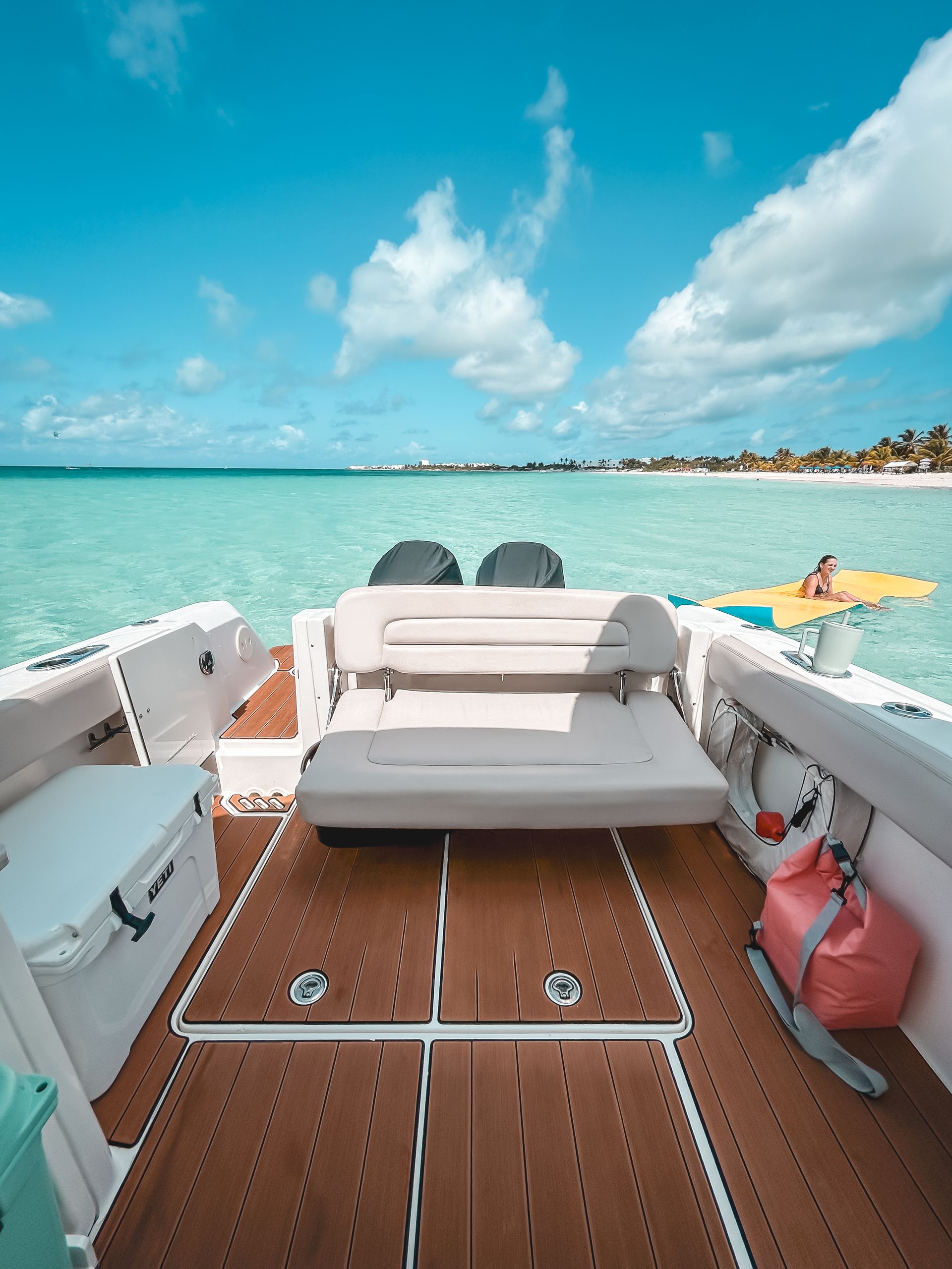 Boat on turquoise water, with a person on a yellow float in the distance. Blue sky with fluffy clouds.