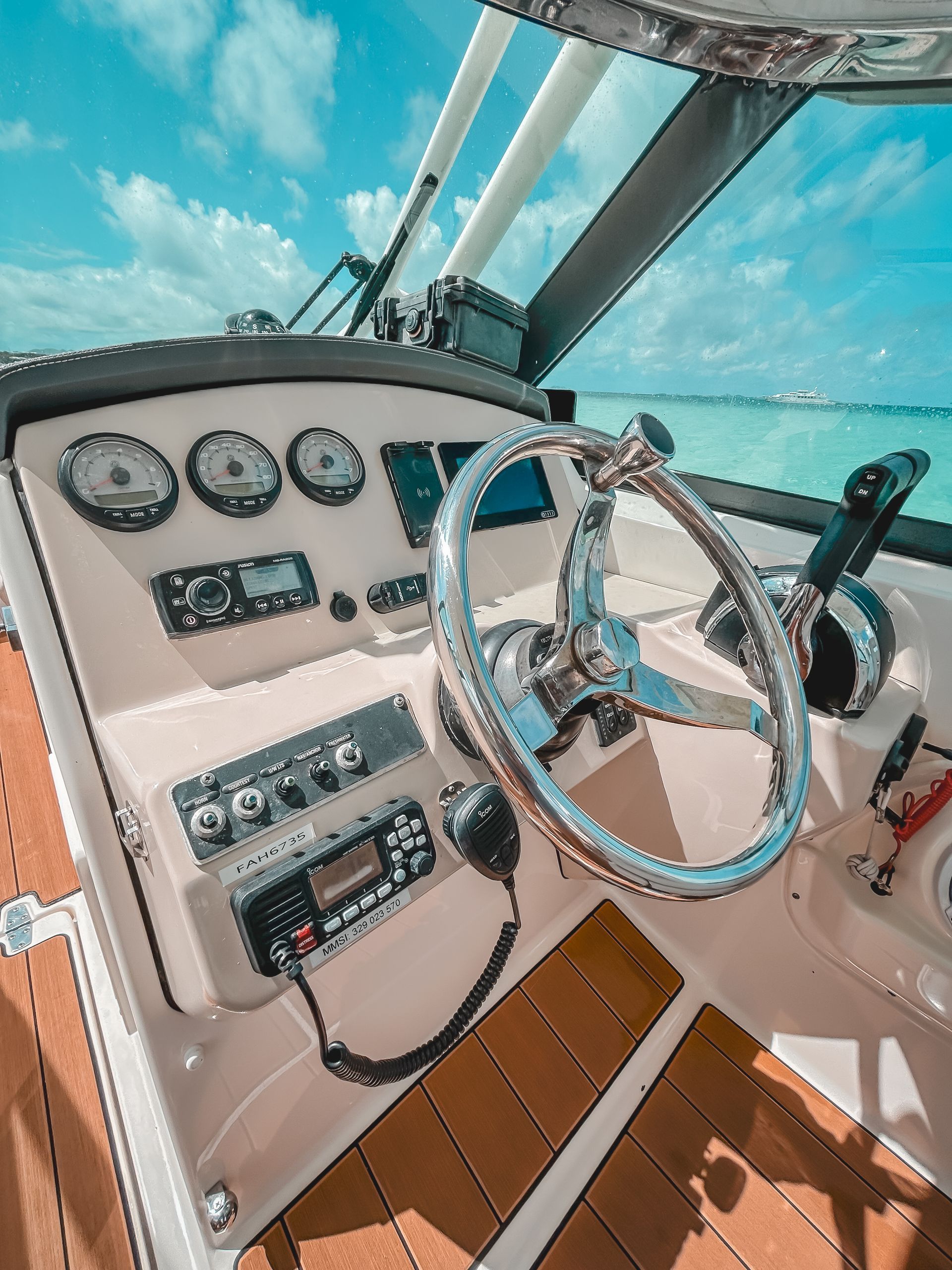 Boat's cockpit with a shiny steering wheel, gauges, radio, and throttle; sunny blue sky in the background.