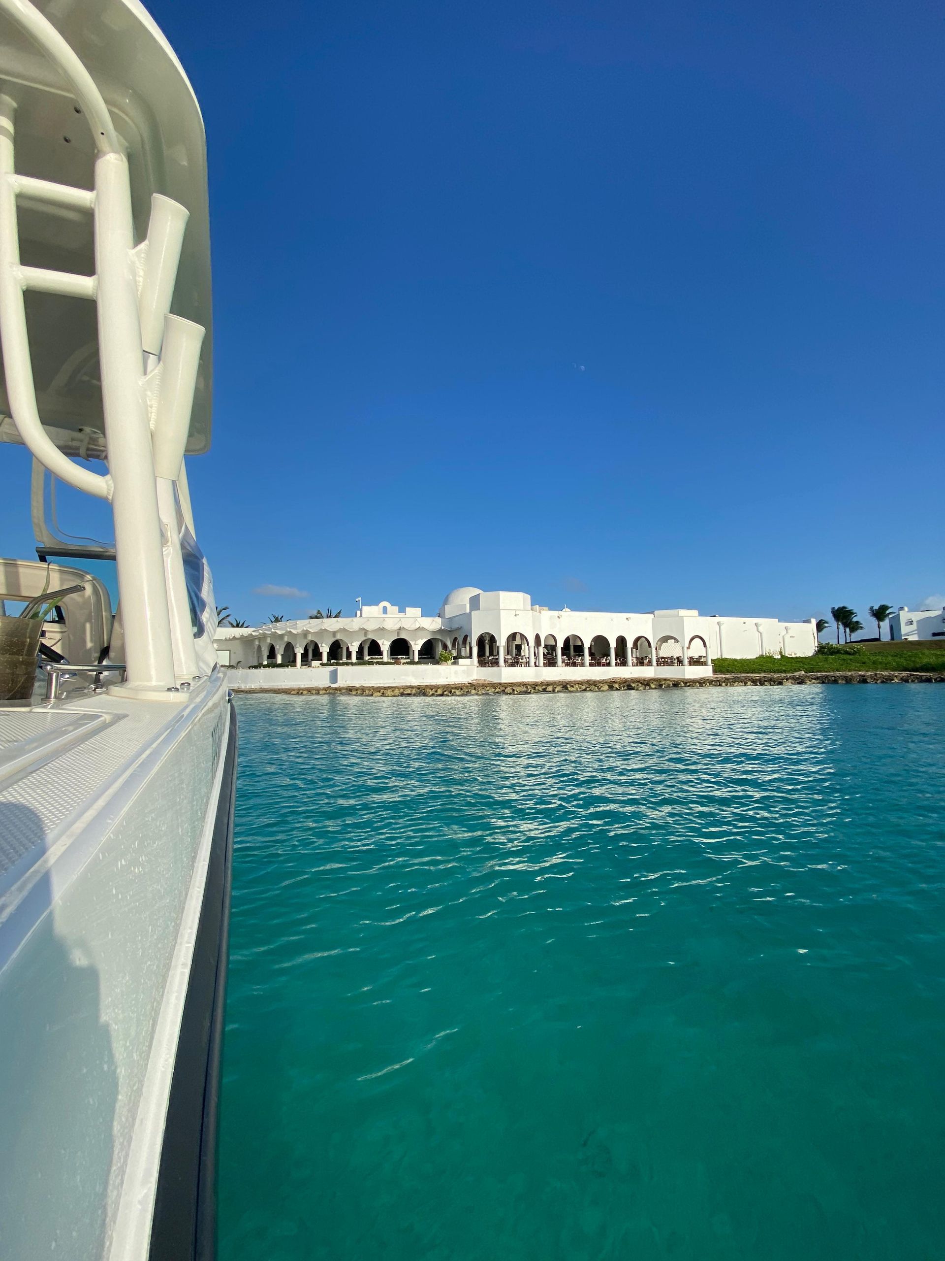 Boat sailing on turquoise water toward a white building under a bright blue sky.