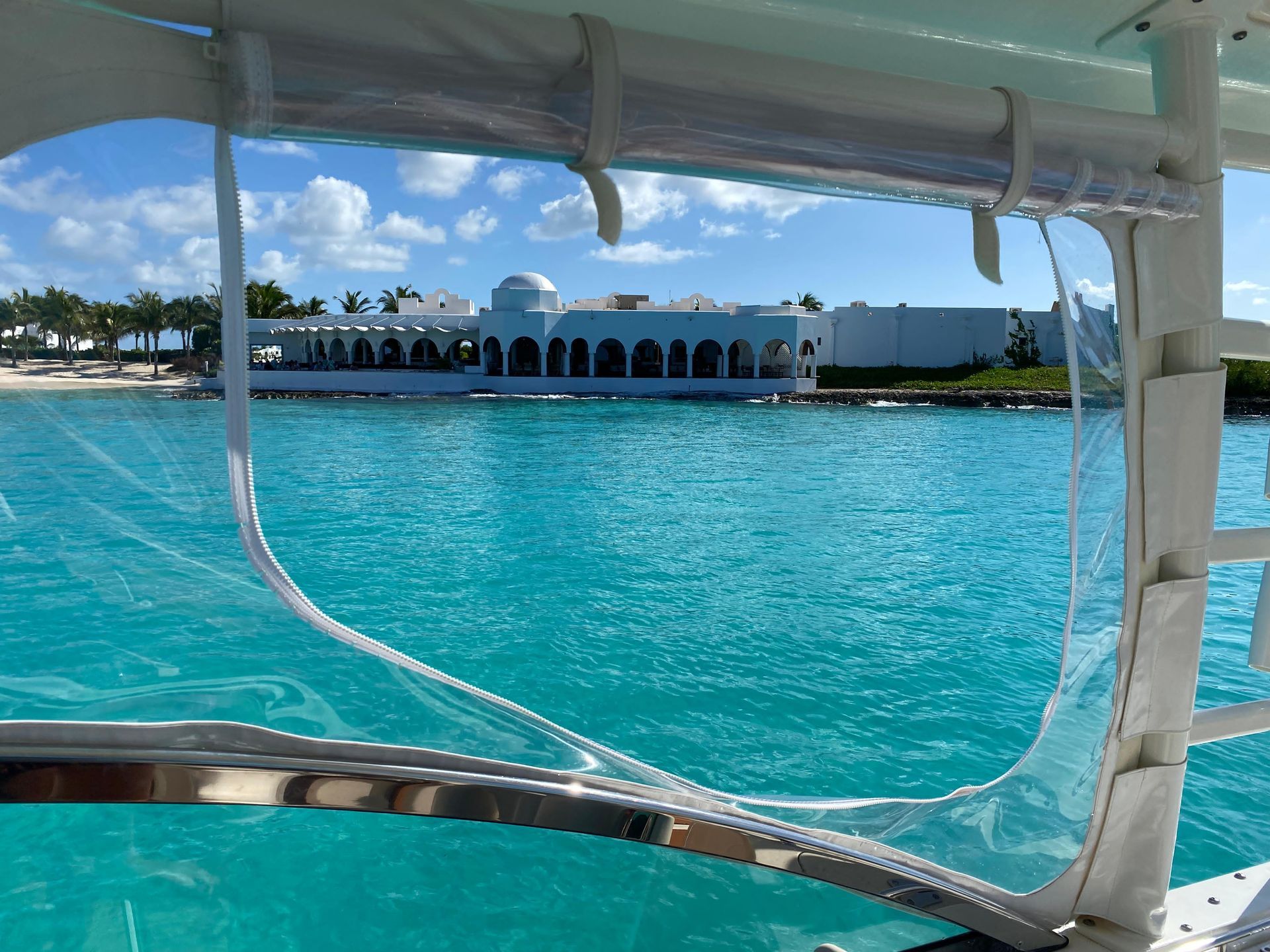 View of a white building on turquoise water through a clear boat window, sunny day.