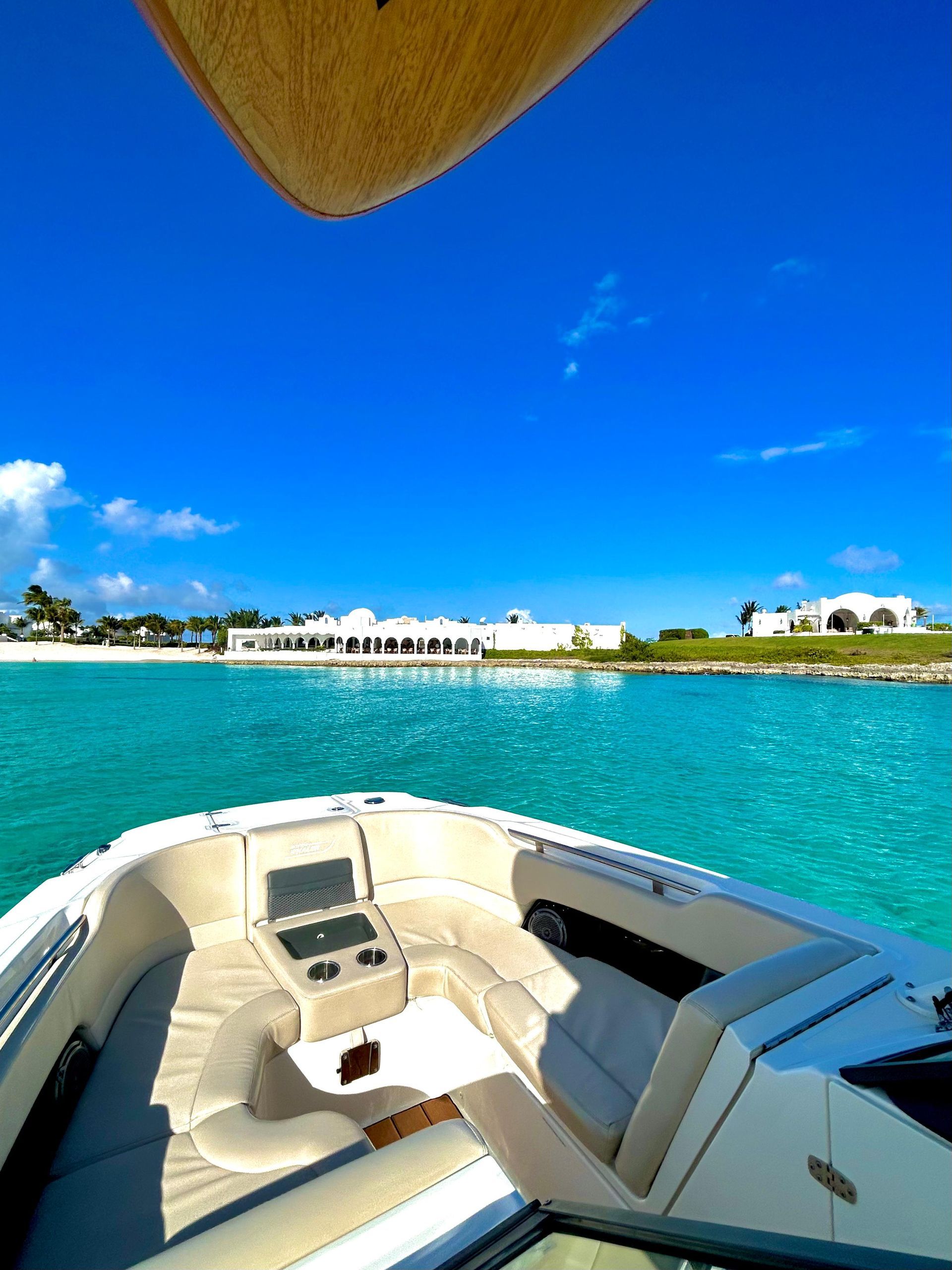 Boat on turquoise water, approaching a white building under a bright blue sky.