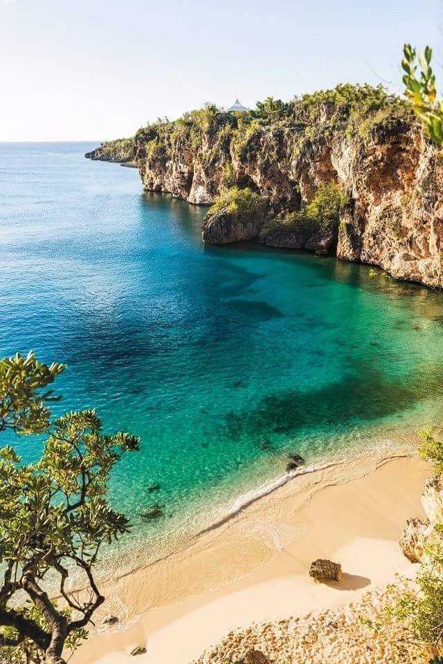Secluded beach with turquoise water, golden sand, and rocky cliffs under a bright blue sky.
