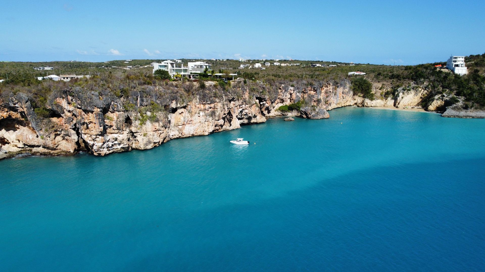 Bright turquoise water, white boat, and rocky cliffs under a clear blue sky.