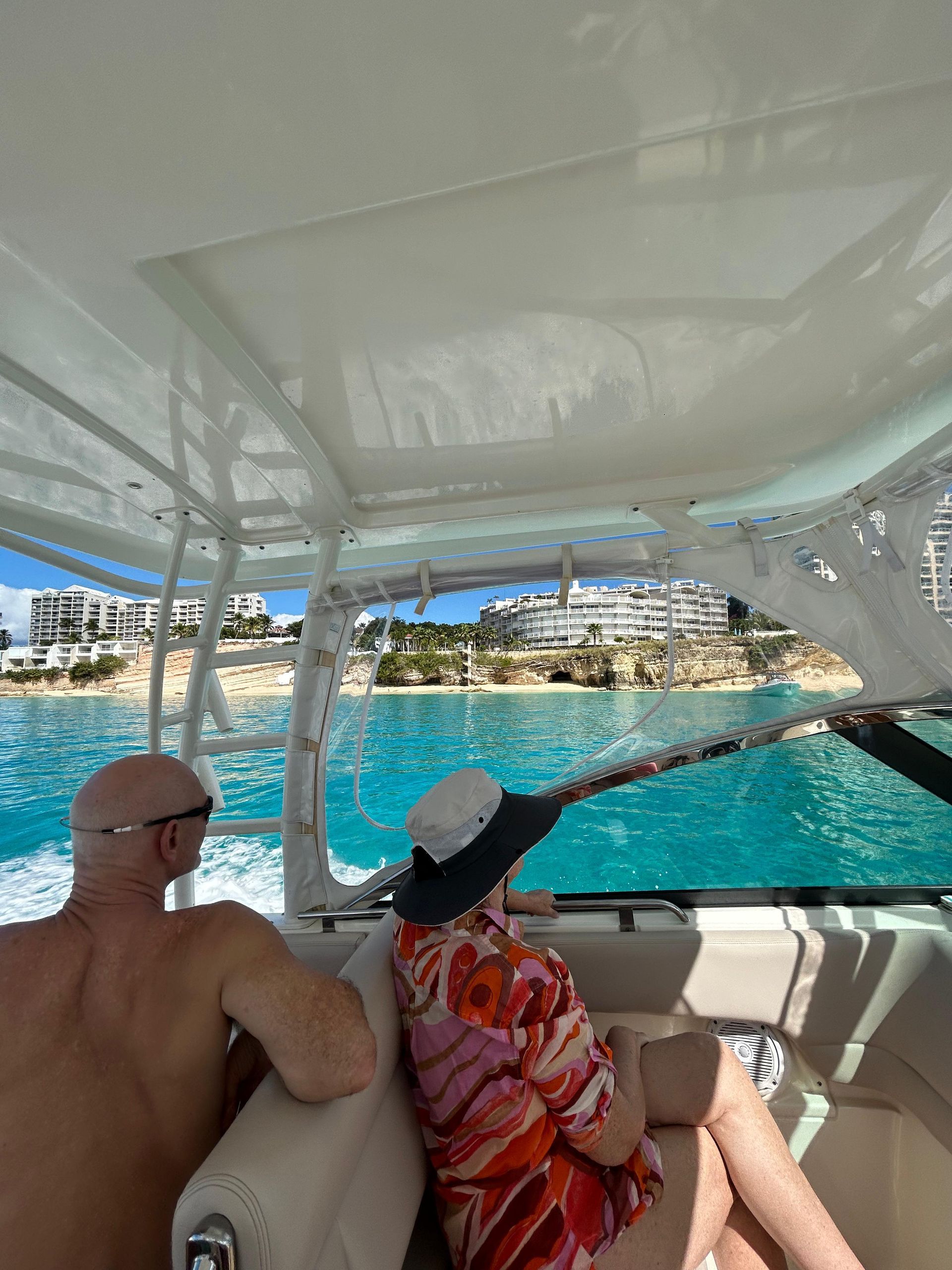 Couple on a boat, gazing at a turquoise sea and shoreline with buildings.