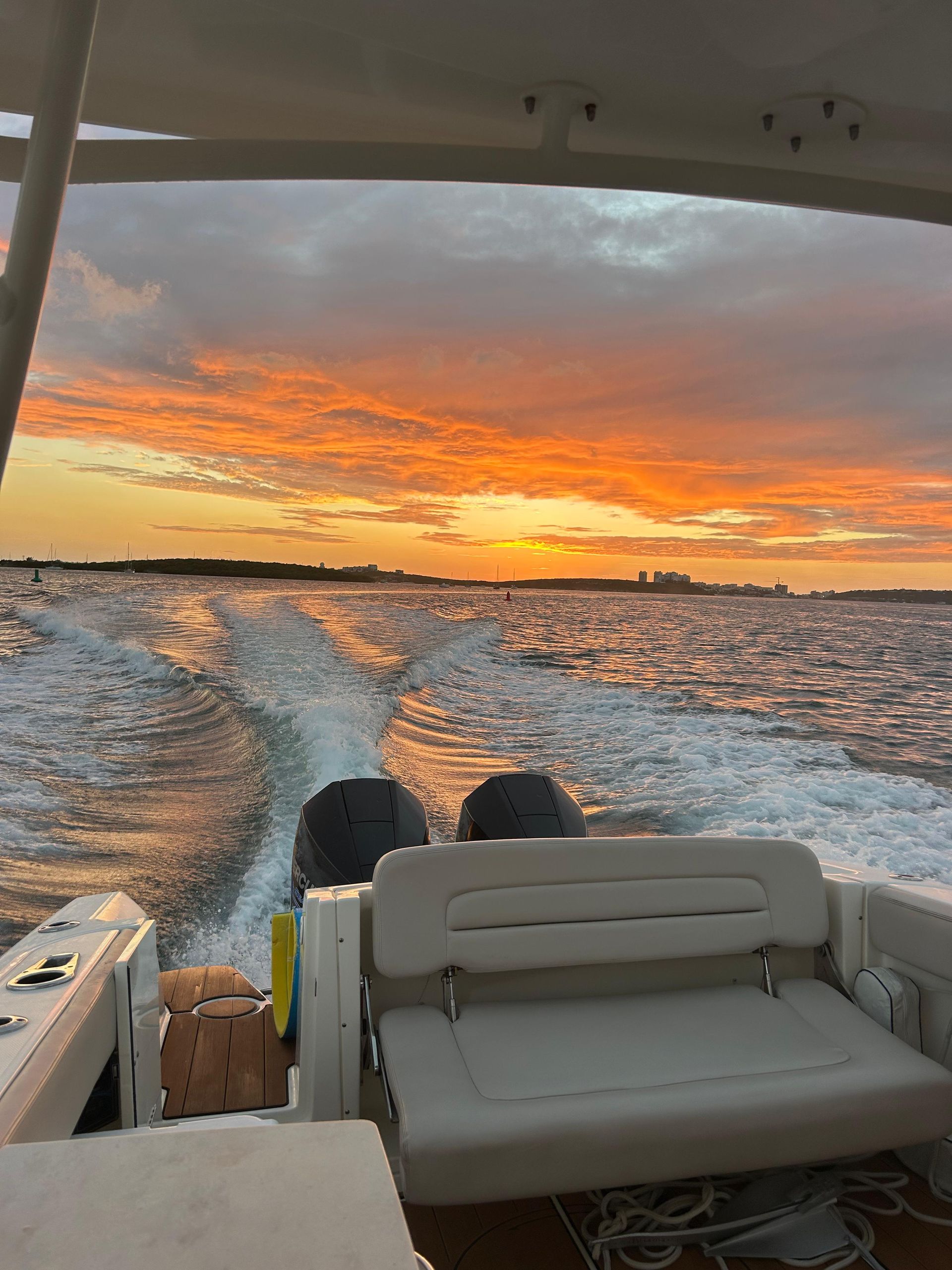Boat speeding across water at sunset, creating wake. Orange and yellow sky.