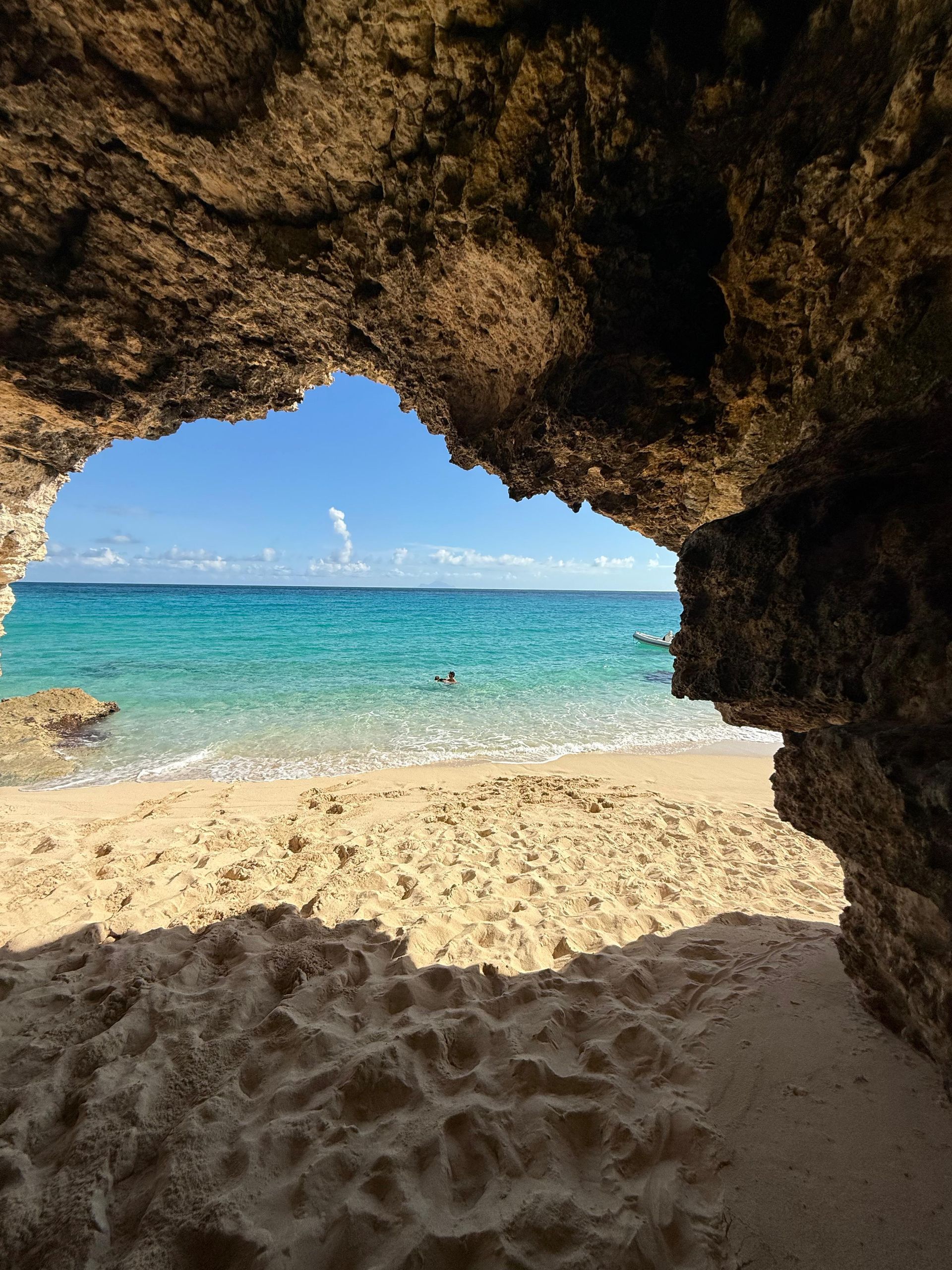 Sandy beach and turquoise ocean framed by a rocky cave opening, blue sky overhead.
