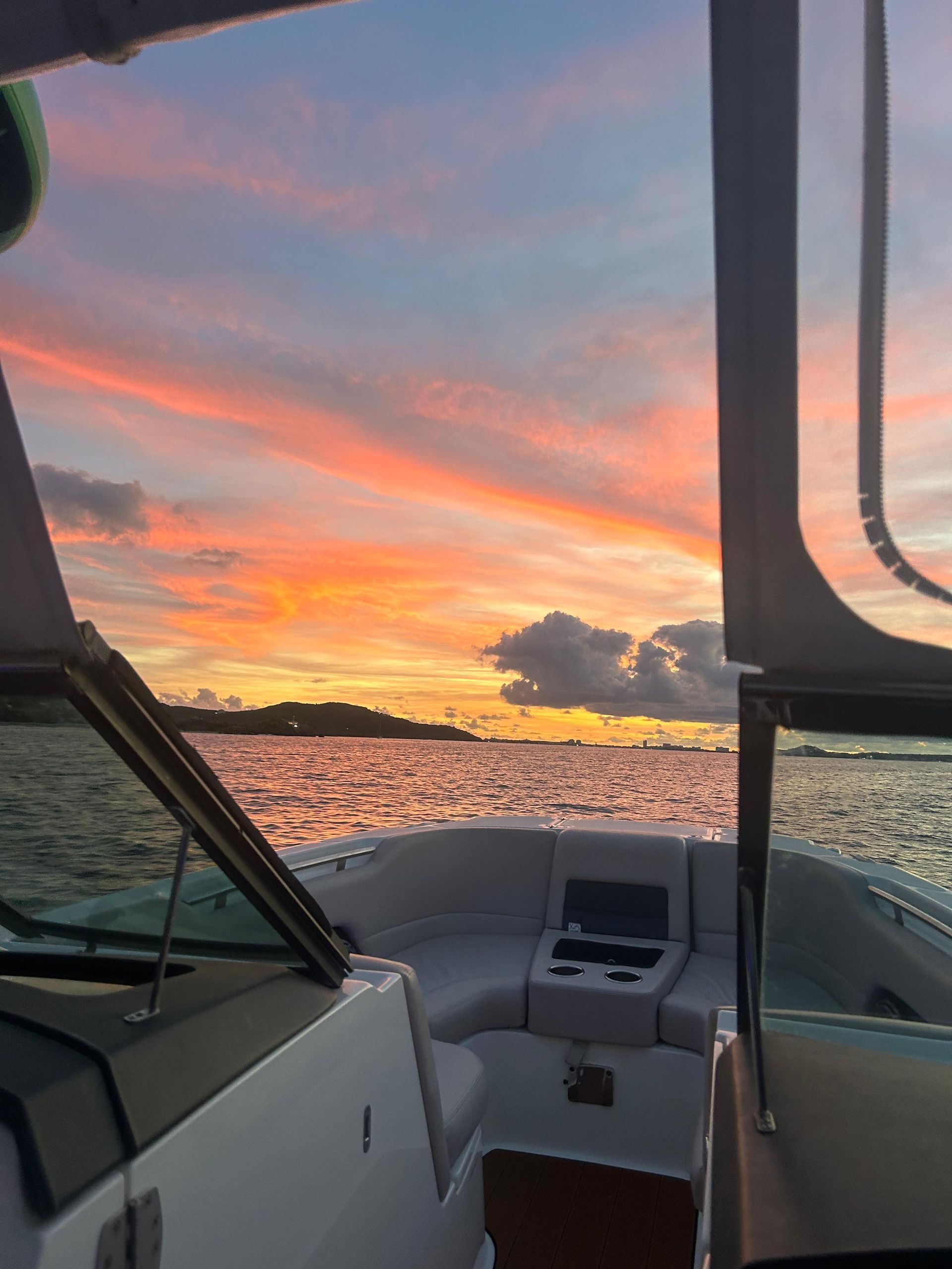 Boat sailing on water at sunset; orange and pink sky reflects on the water.