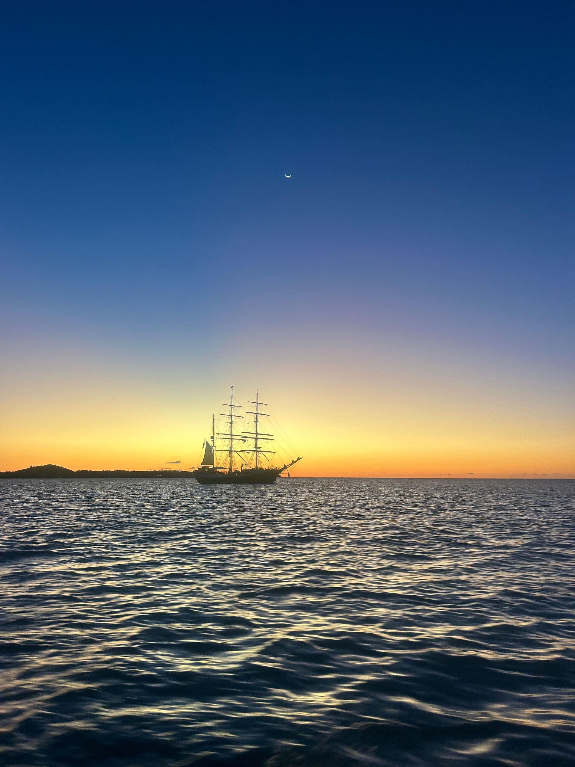 Silhouette of a tall ship on the ocean at sunset, with a gradient sky of blue and orange.