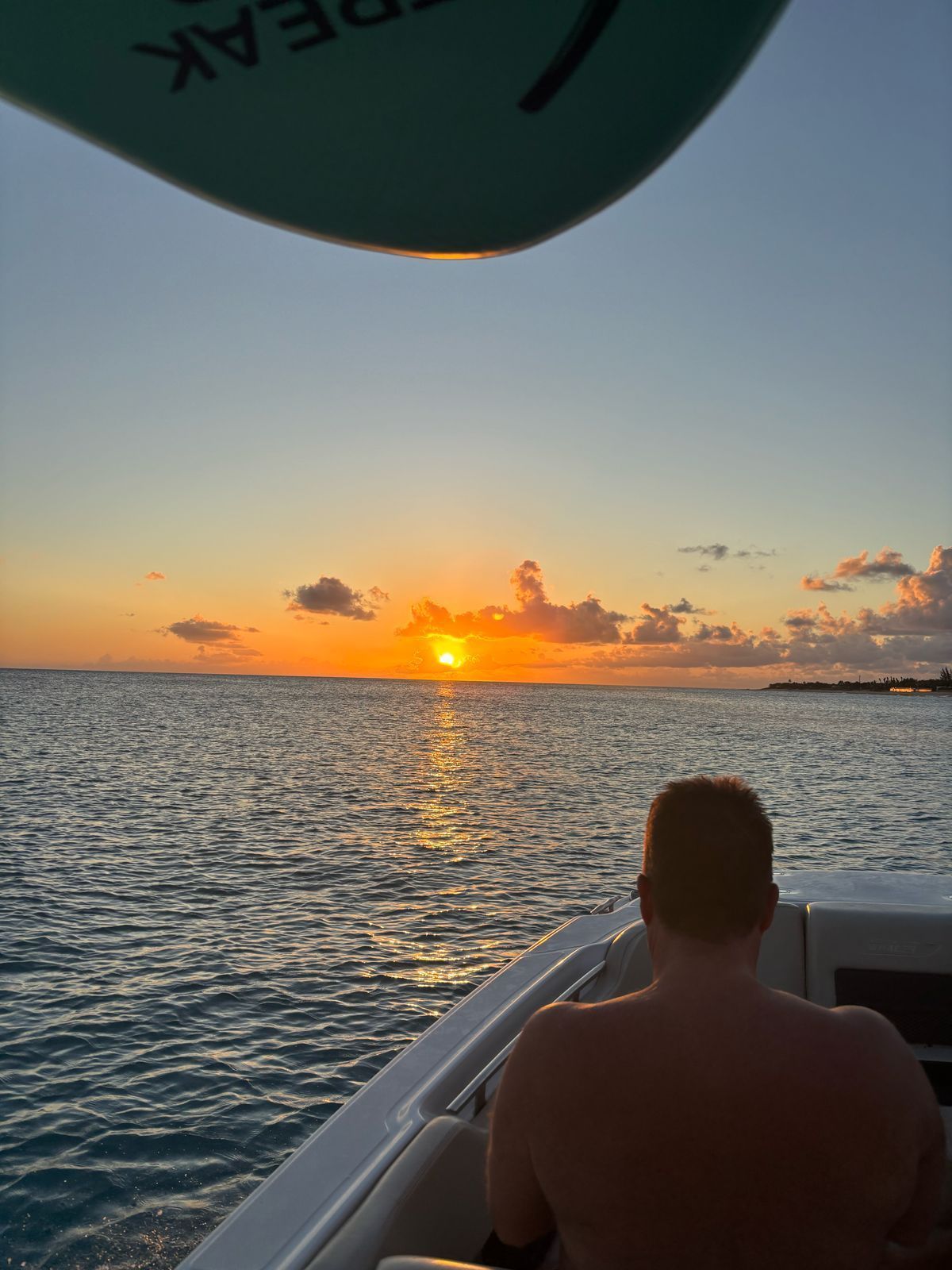 Man on a boat watching sunset over the ocean. Warm colors, calm waters.