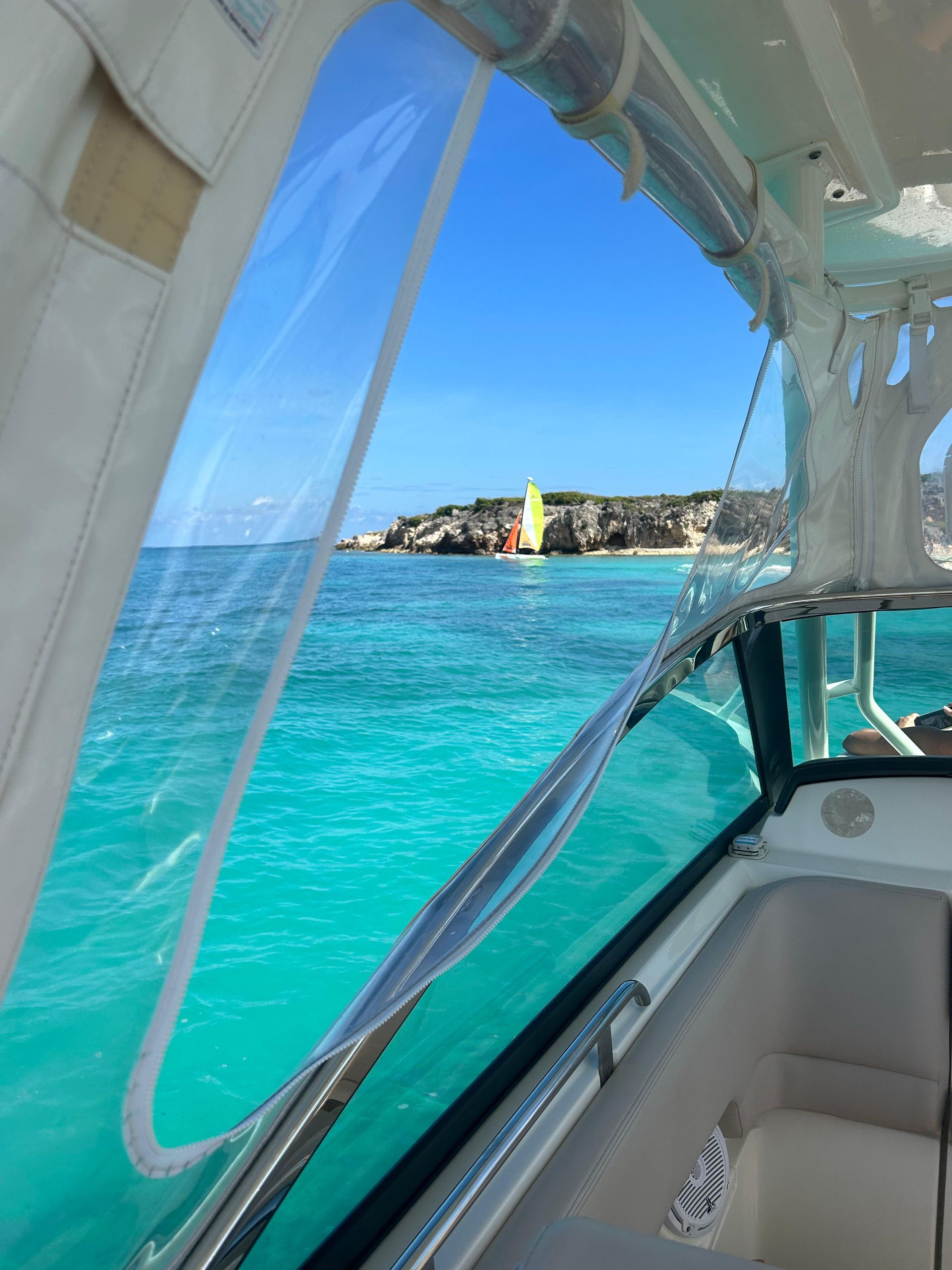 View from a boat window of turquoise water, a yellow and red structure on a small island, and blue sky.