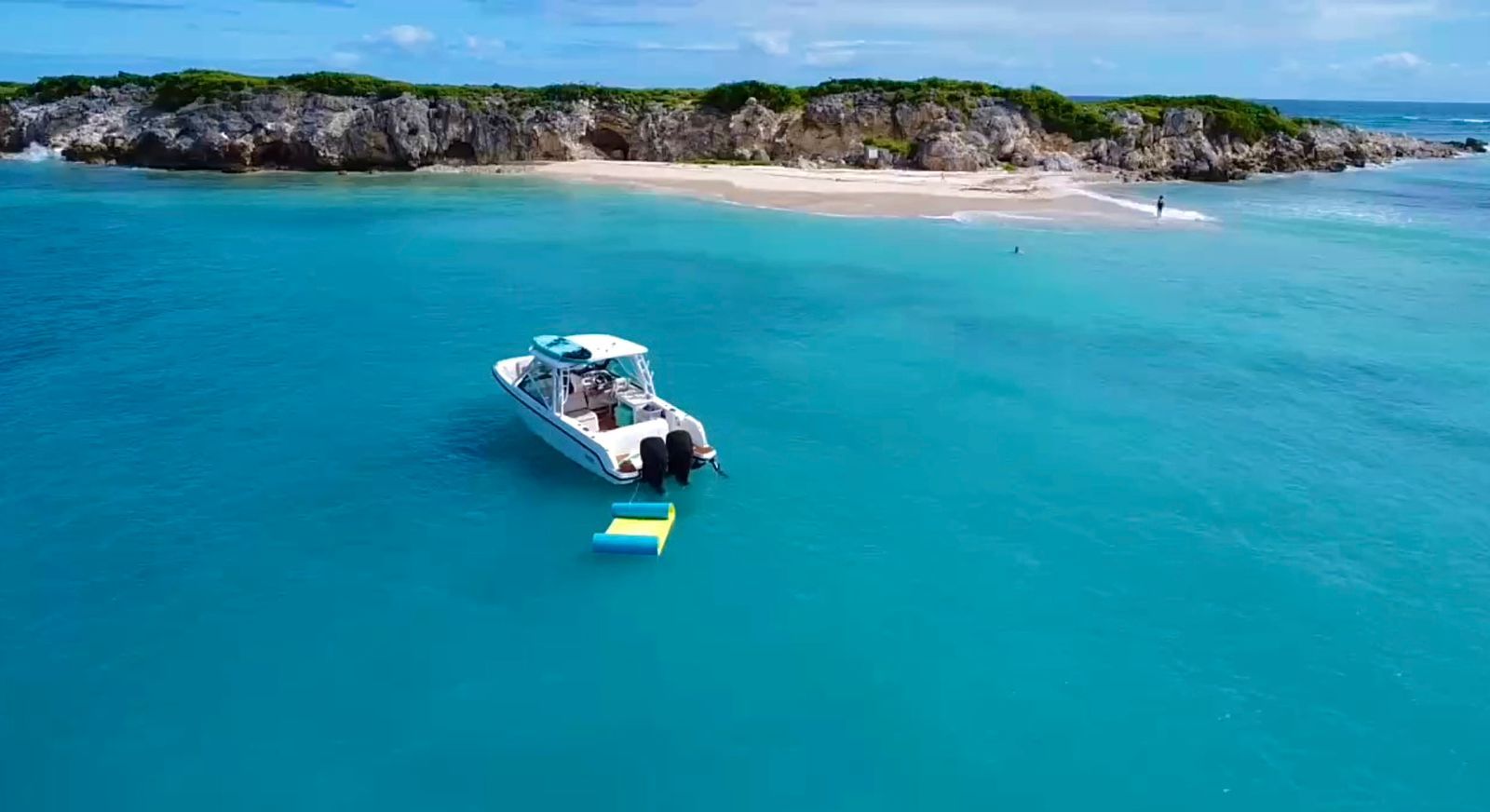 A white boat in turquoise water near a small island with people, sunny day.
