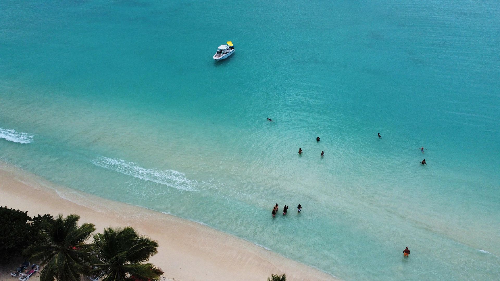 Aerial view of beach with turquoise water, people swimming, and boat offshore.
