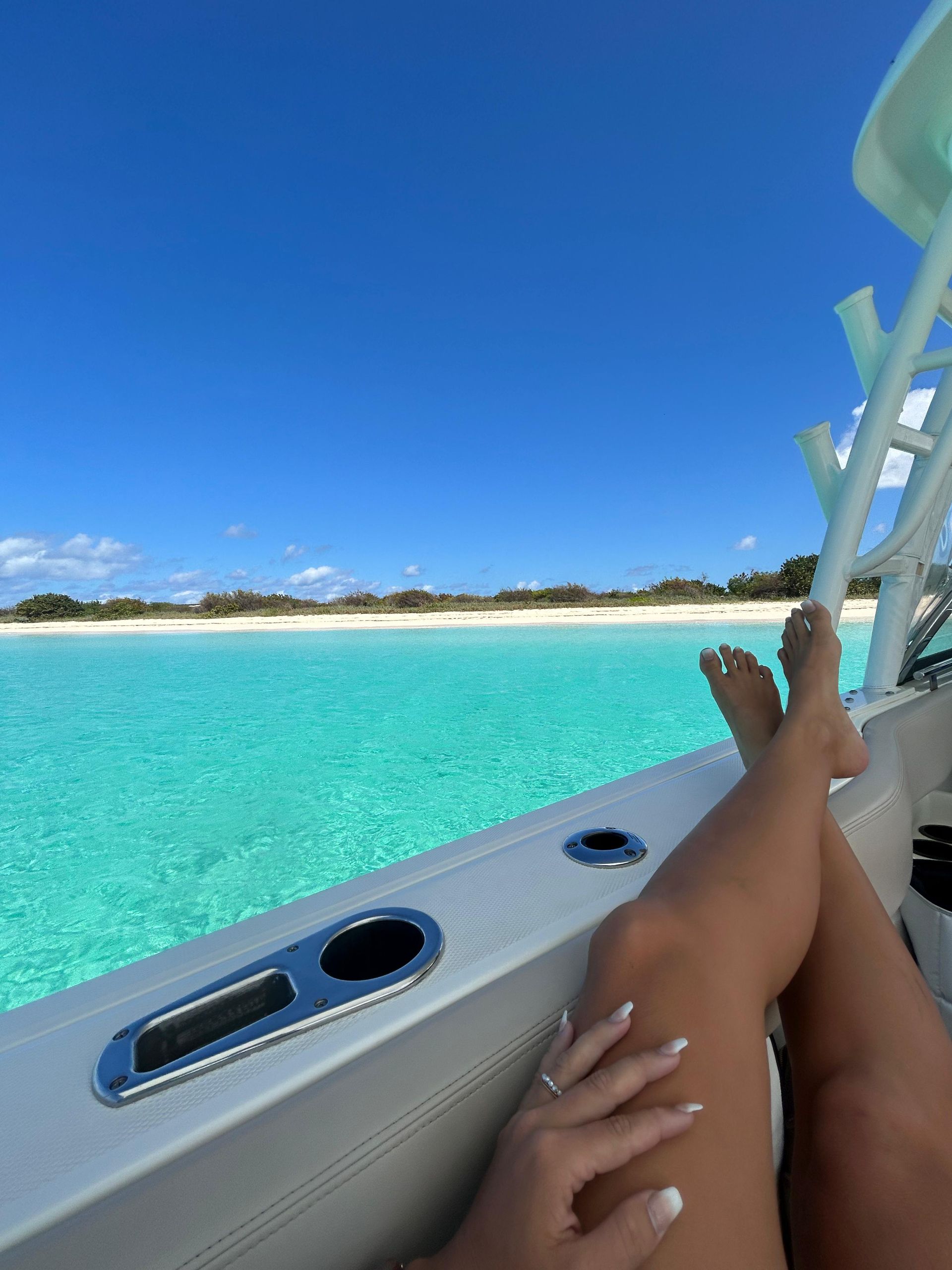 Woman relaxing on a boat with turquoise water and a beach in the background.