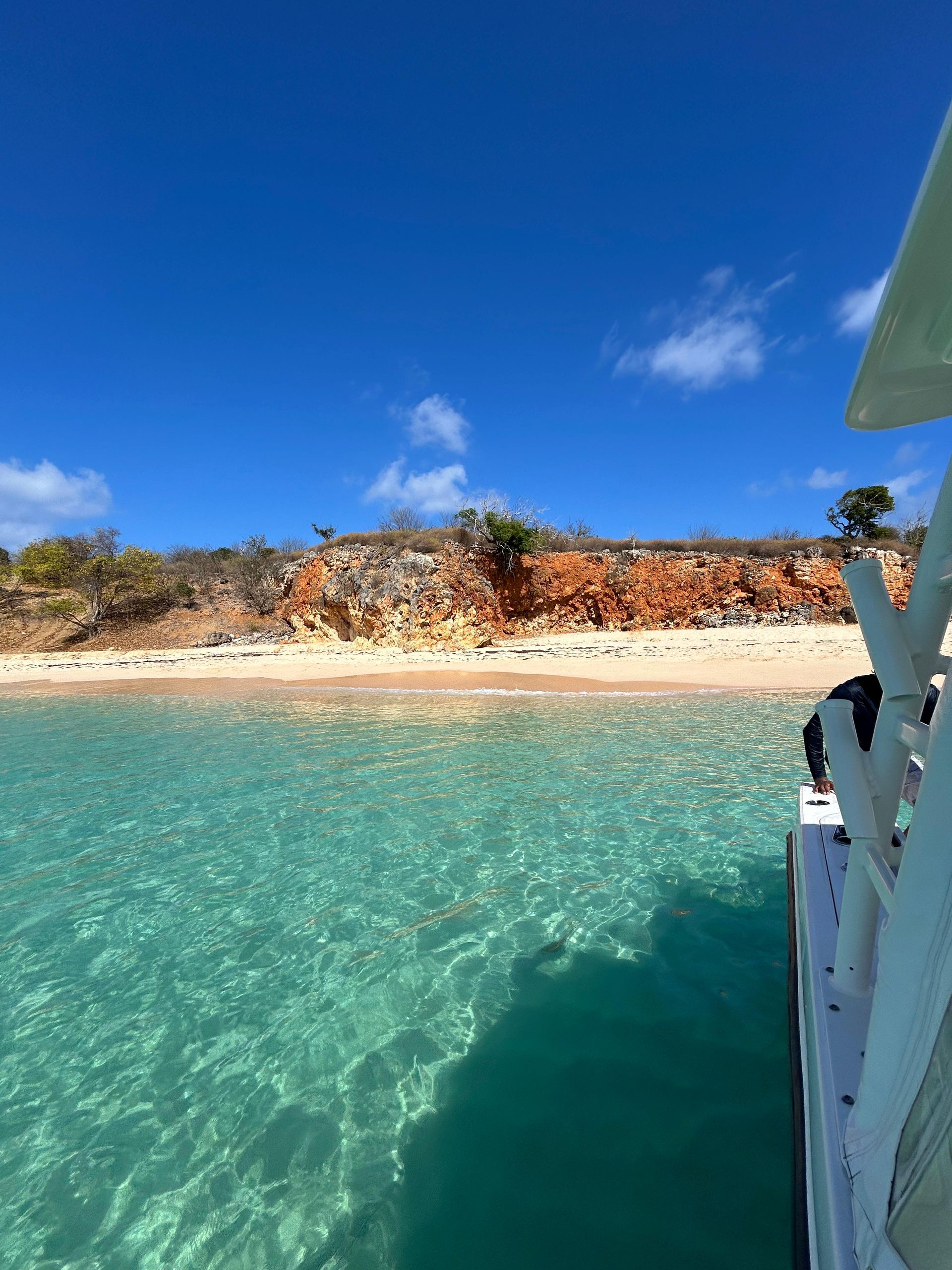 Bright turquoise water with white boat and red-brown cliffs against a blue sky.