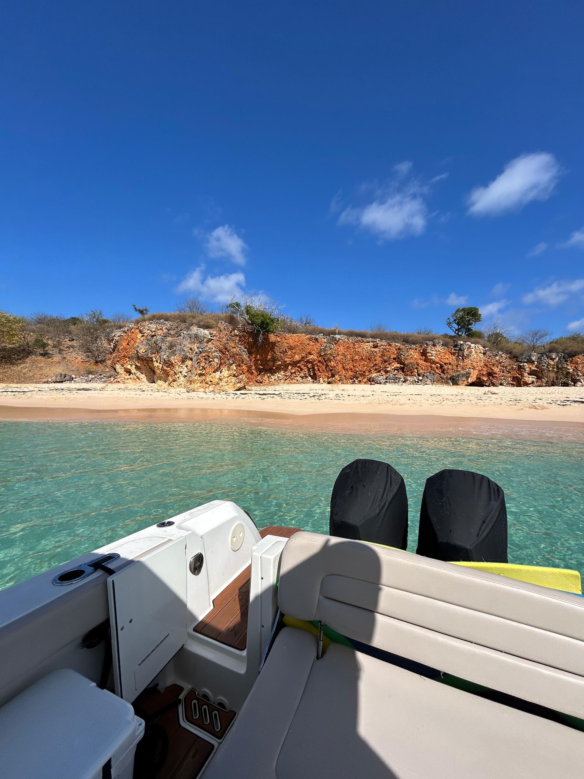 Boat on turquoise water near a red-cliffed beach under a blue sky.