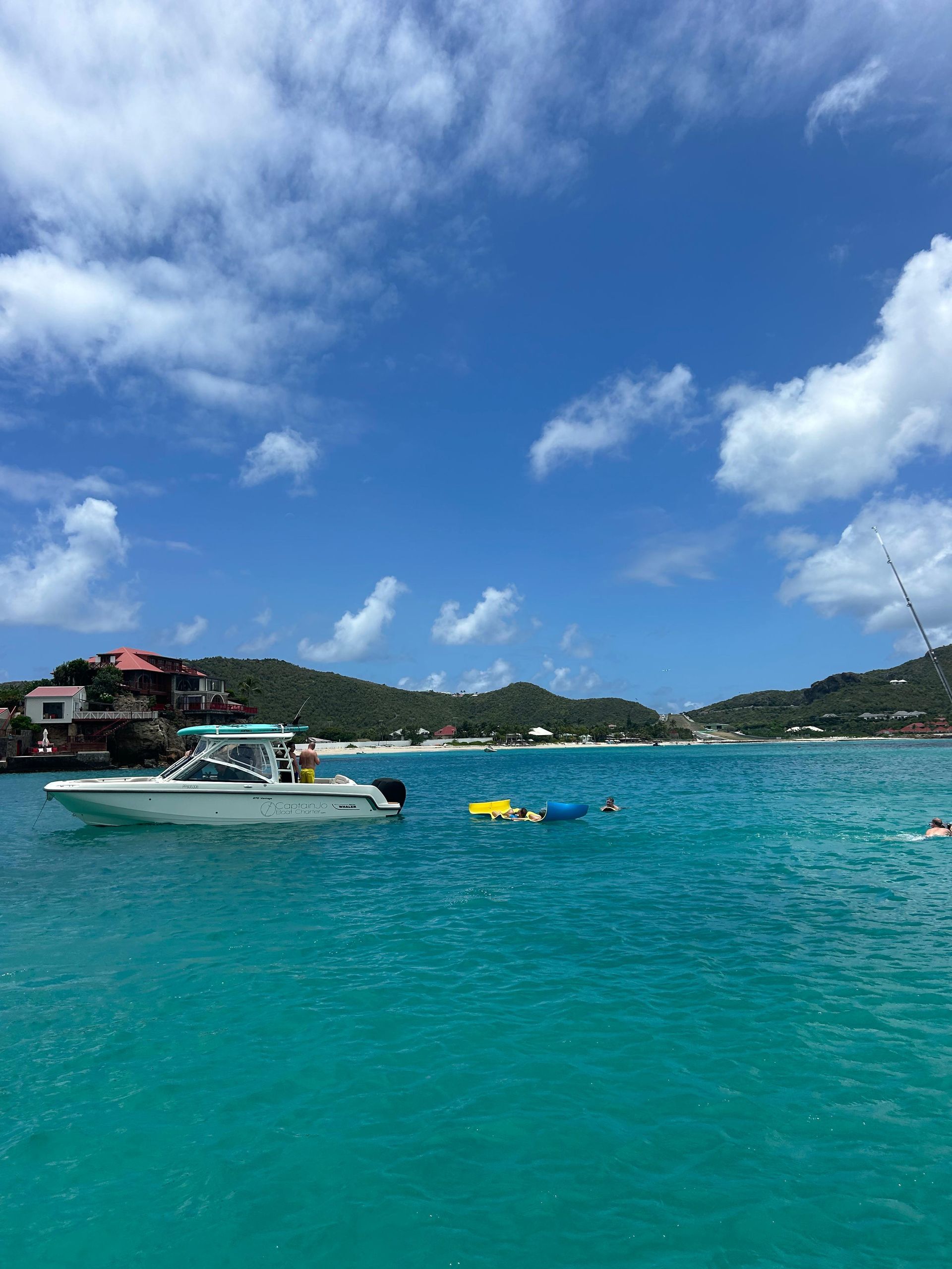 Boat on turquoise water near green hills under a blue sky with clouds.