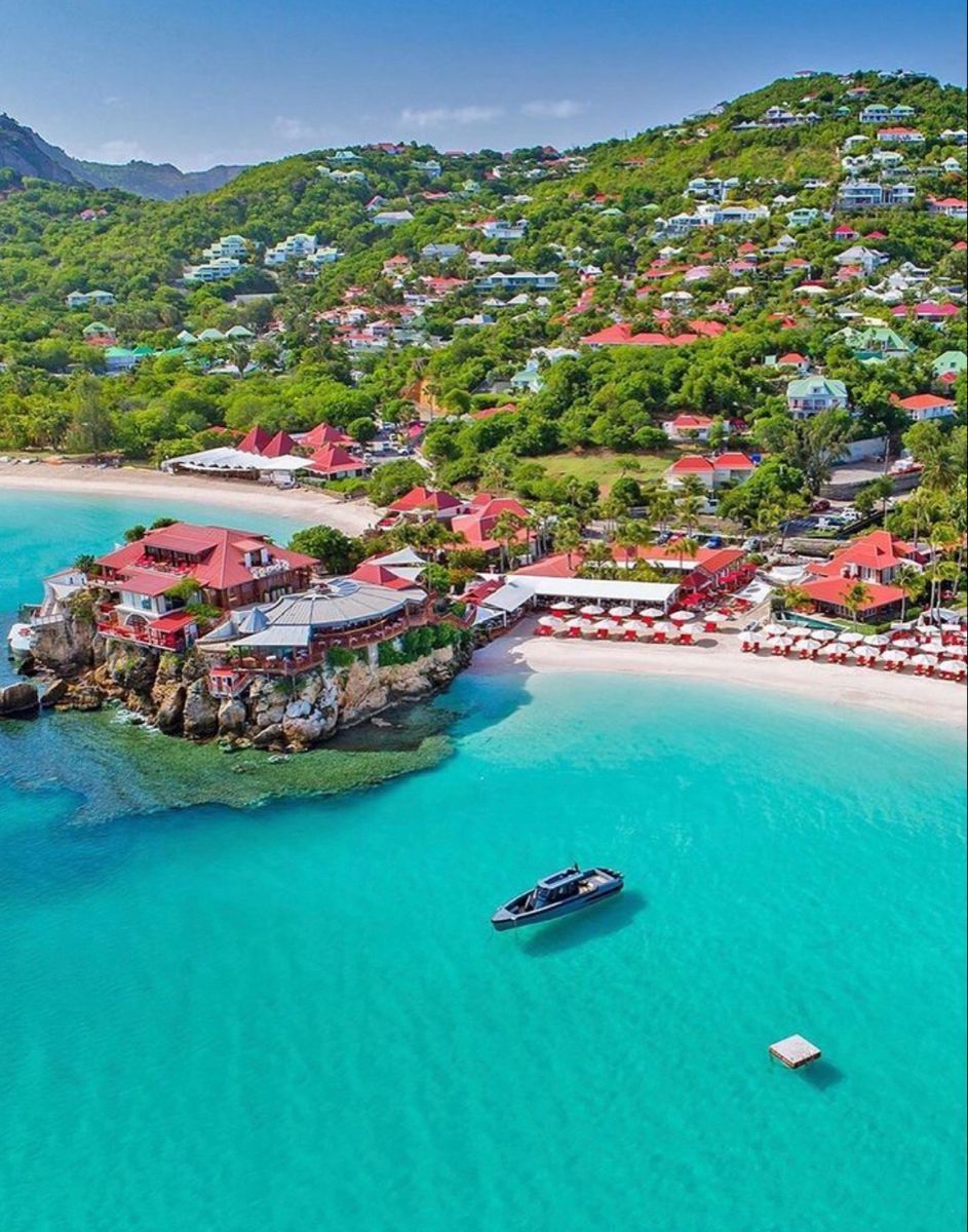 Turquoise water, white sand beach, red-roofed buildings on a cliff, hillside houses, St. Barts island.