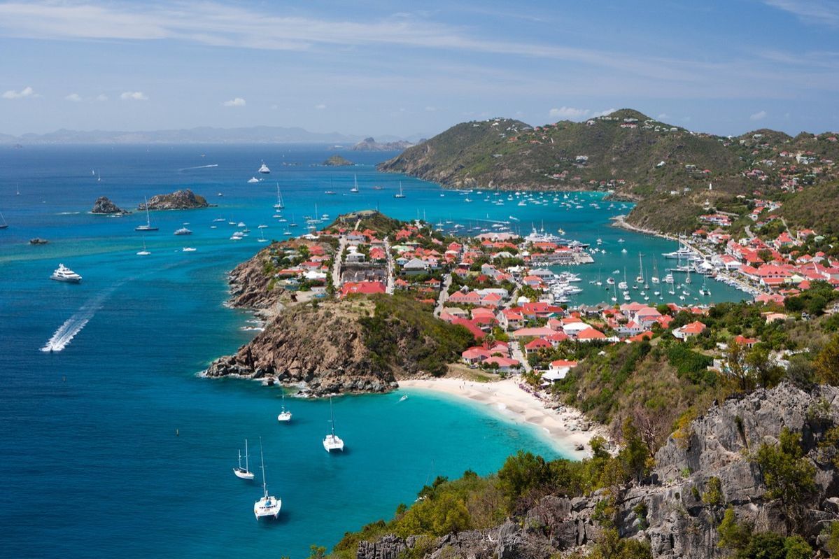 A scenic view of a coastal town in Saint Barthélemy, with boats on turquoise water and red-roofed buildings.