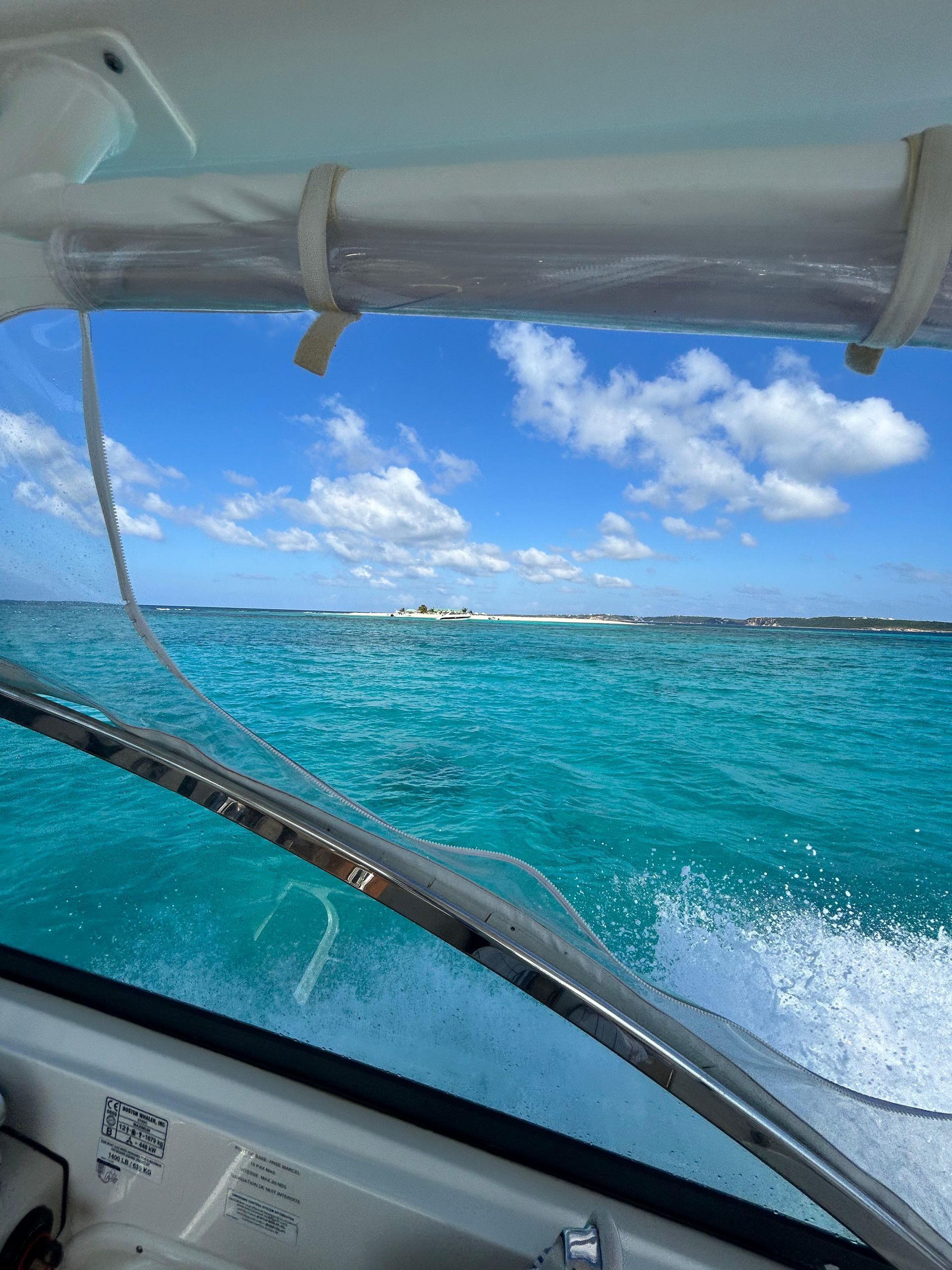 Boat sailing on turquoise water toward a distant island under a blue sky with clouds.