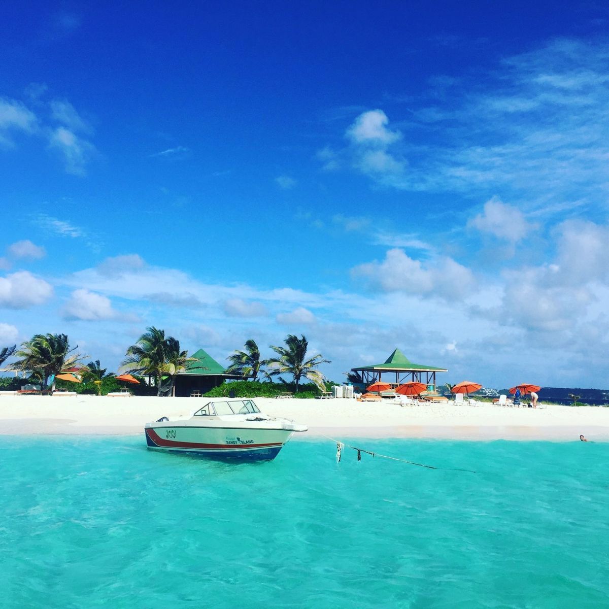 Boat on turquoise water near a white sand beach under a bright blue sky.
