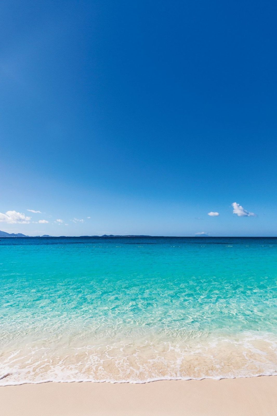 Bright blue sky over a turquoise ocean, meeting a white sandy beach on a sunny day.