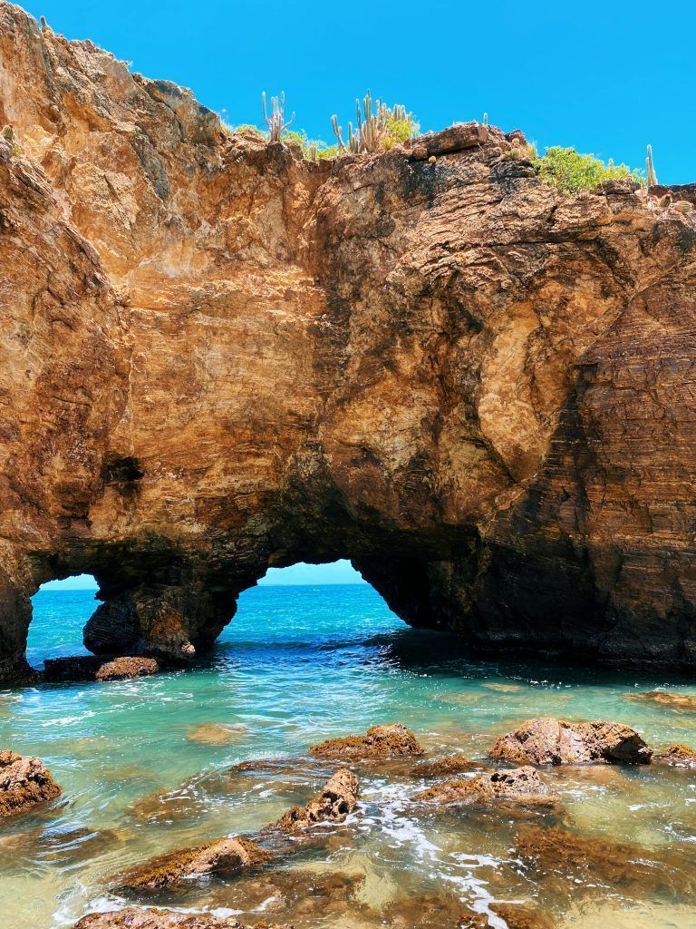 Rocky archway over turquoise water under a blue sky.