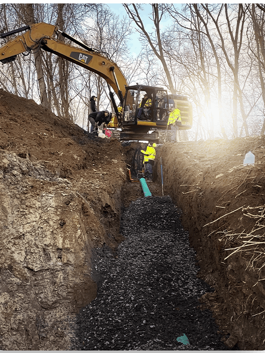 A cat excavator is digging a trench in the woods.