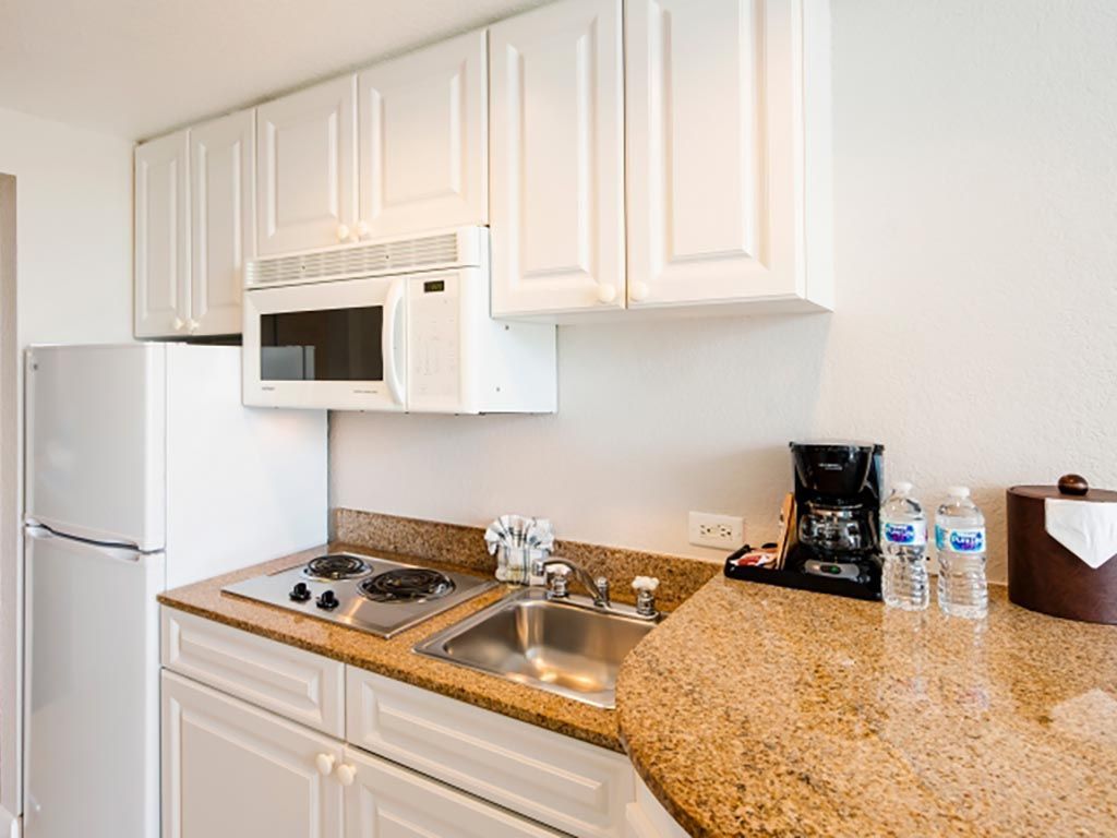 Small kitchenette with white cabinets, appliances, and a speckled countertop.