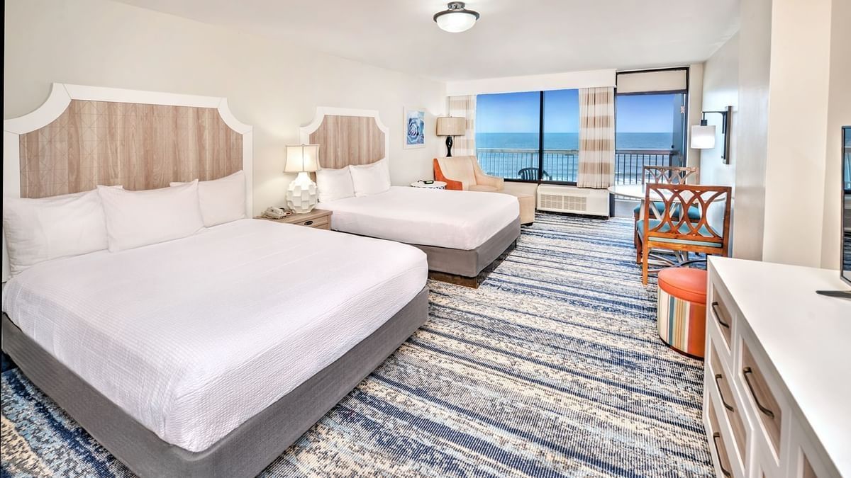 Hotel room with two beds, ocean view, white and blue decor, balcony access.