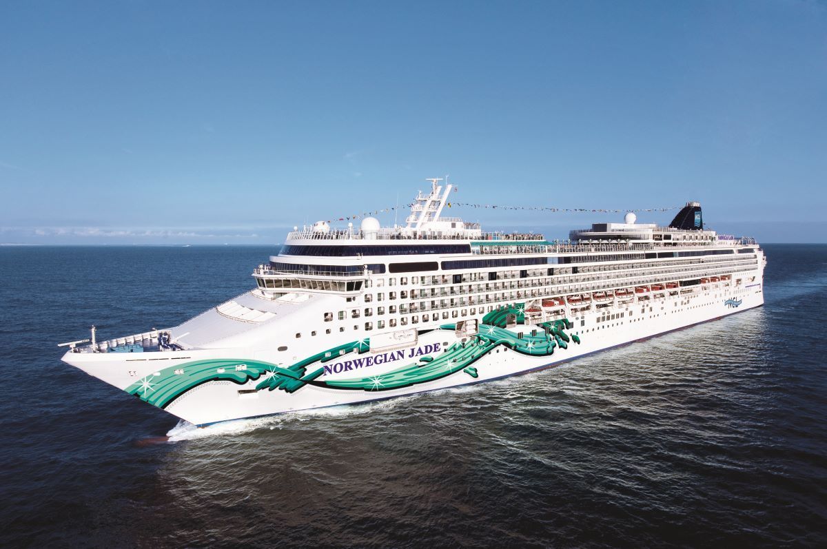 Large cruise ship, white with green dragon art, sailing on blue water under a clear sky.