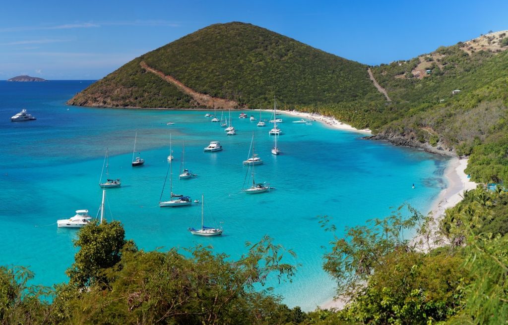 Bright turquoise bay with boats, white sand beach, and lush green hills.
