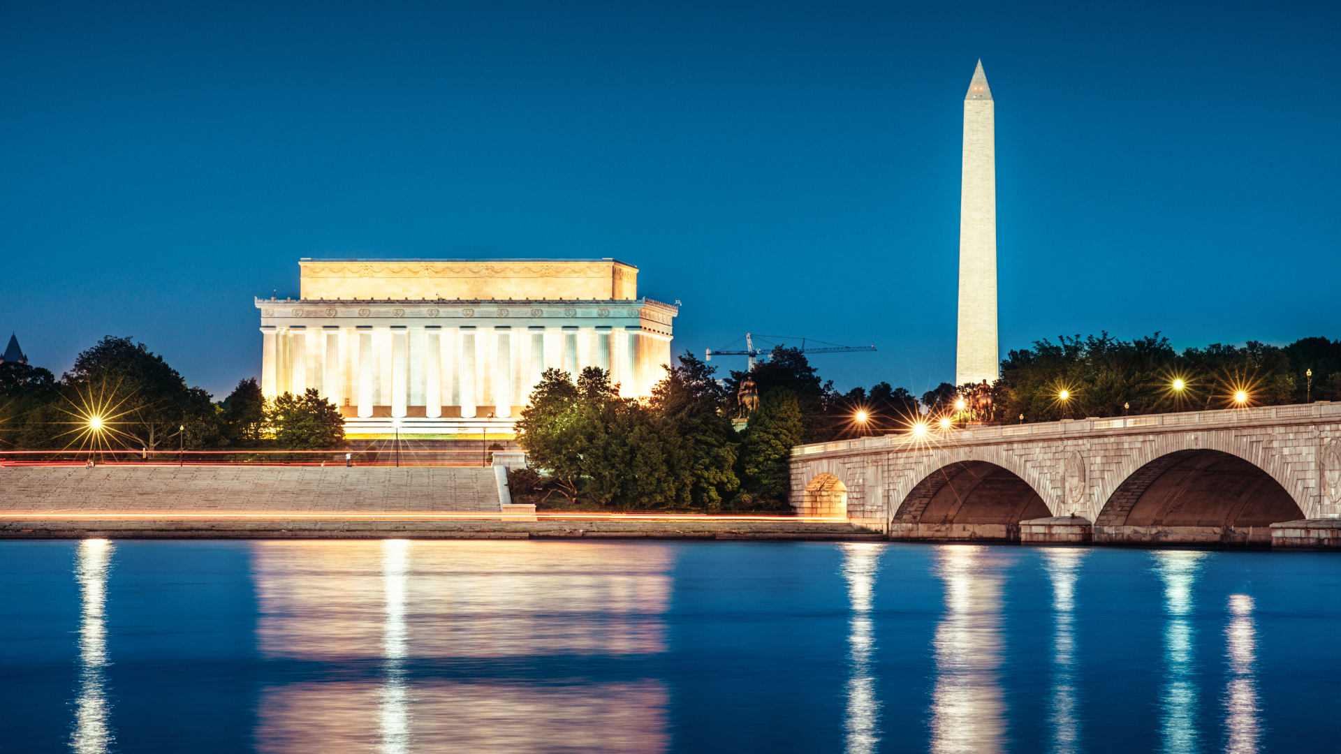 Lincoln Memorial, Washington Monument, and bridge reflected in water at night.
