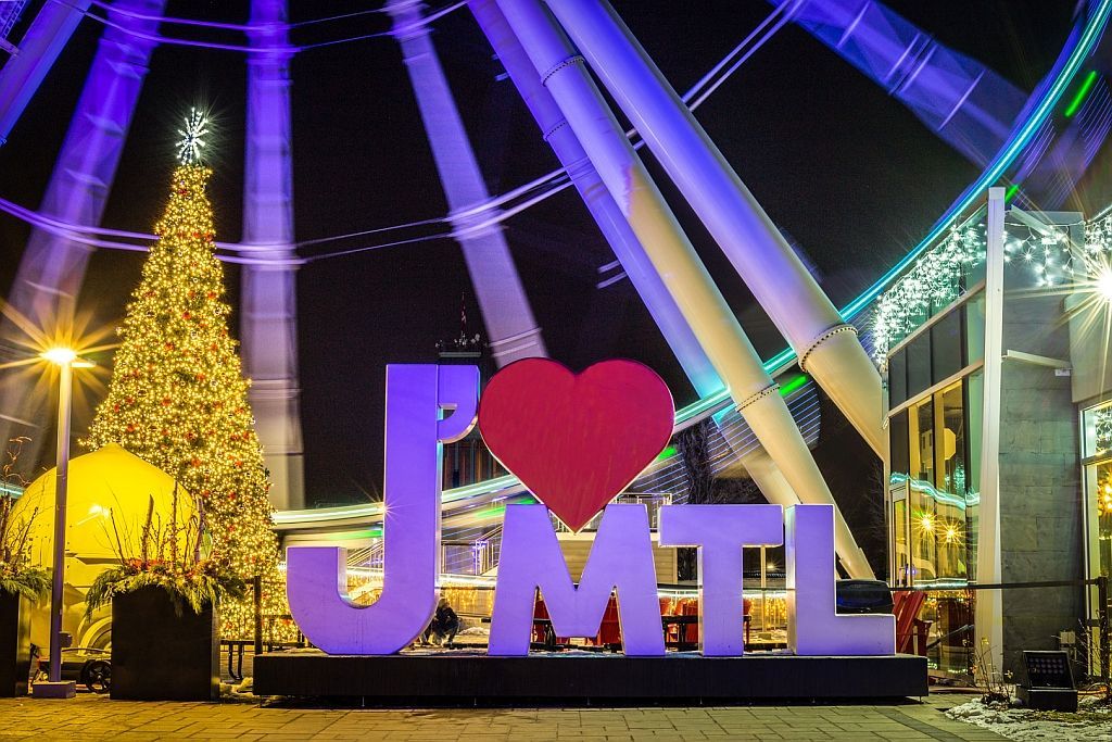 Waterfall illuminated with pink and blue lights at night, with snow and a bridge.
