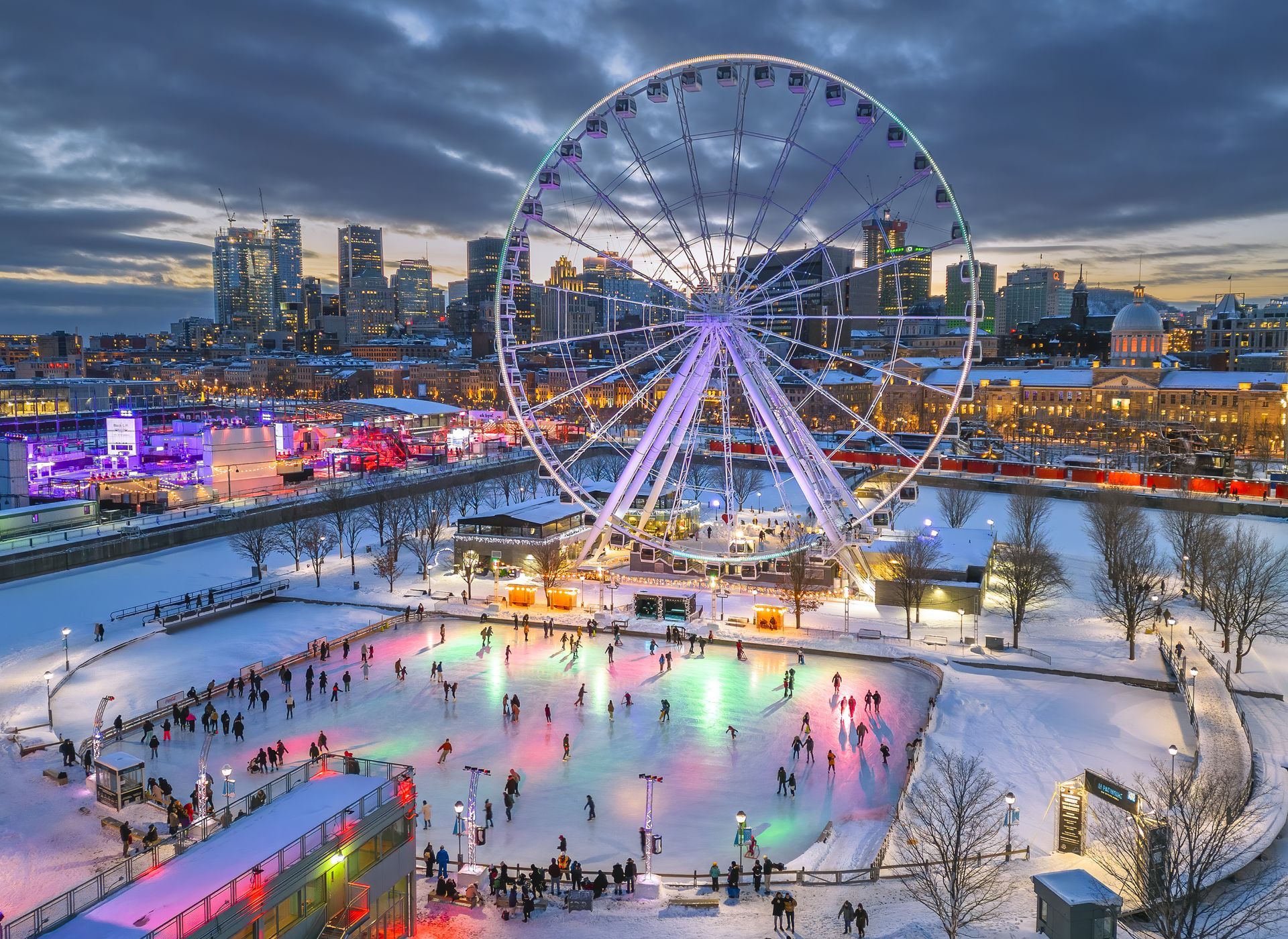 Winter city skyline with a lit Ferris wheel and people skating on an ice rink at dusk