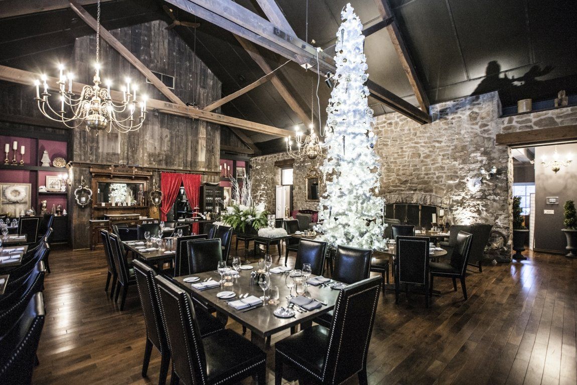 Restaurant interior: dark wood floors, stone walls, large lit Christmas tree, tables set for dining.