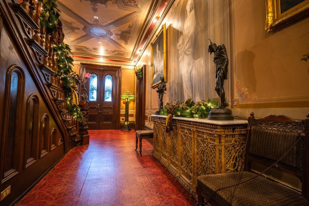Elegant hallway with red tile floor, carved wood staircase, ornate décor, and warm lighting