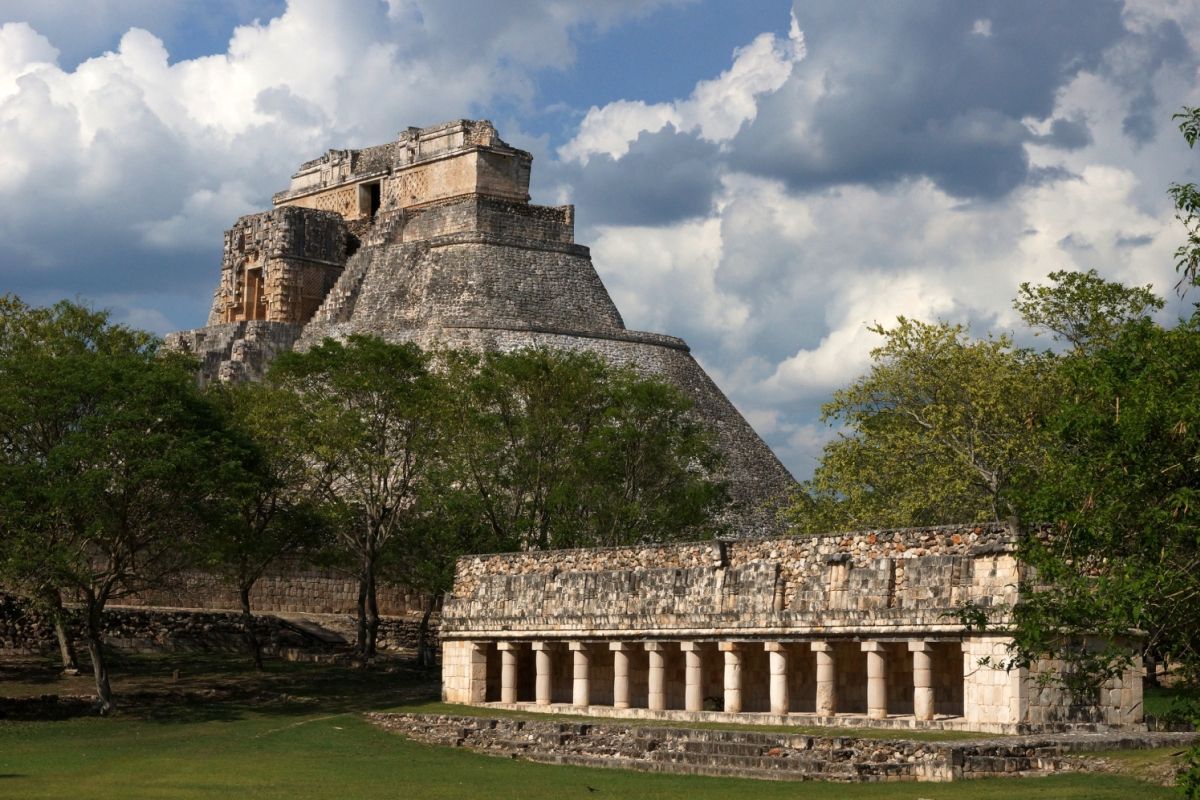 Pyramid and building ruins at Uxmal, Mexico, with green trees and blue sky.