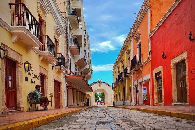 Cobblestone street lined with colorful buildings in Campeche, Mexico; a person sits on a bench.