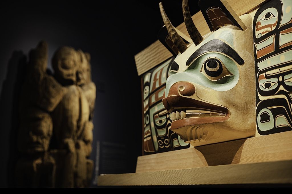 Totem pole with detailed carved animal face, other totem in soft focus background.