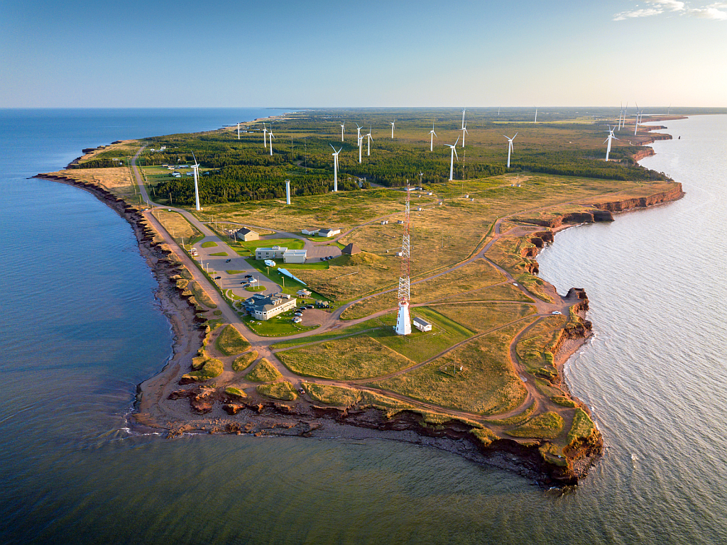 Two red Adirondack chairs face a calm bay, with red cliffs and trees in the background.