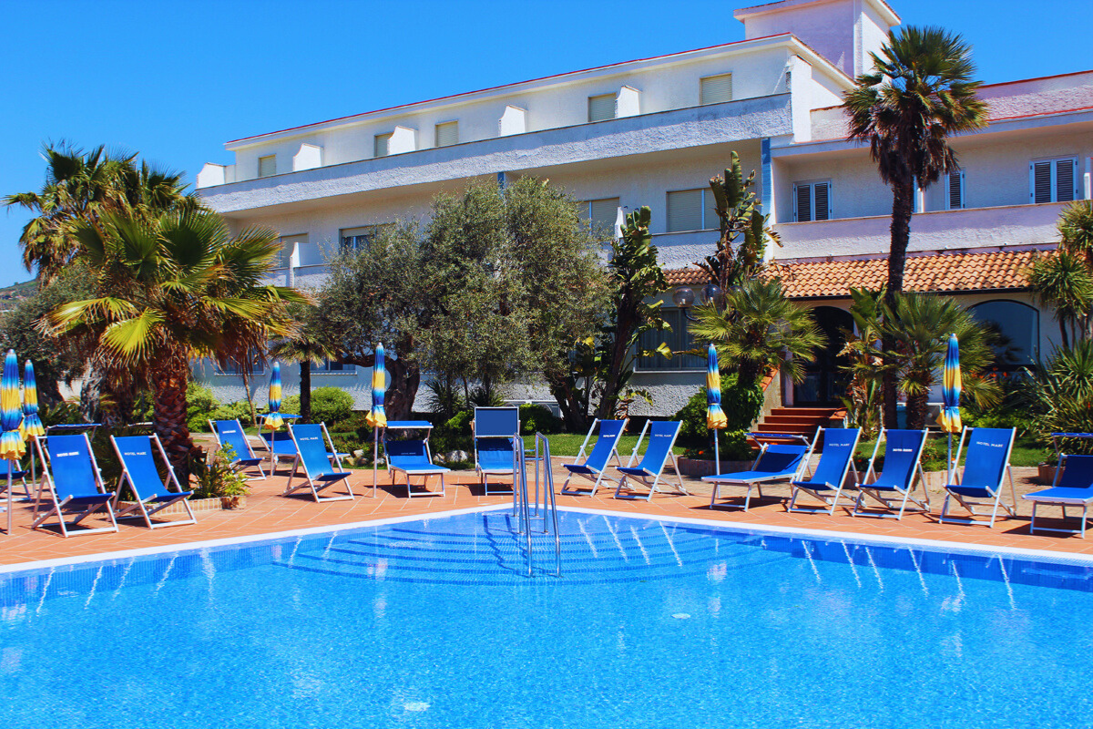 Hotel with blue pool, lounge chairs, and palm trees on a sunny day.